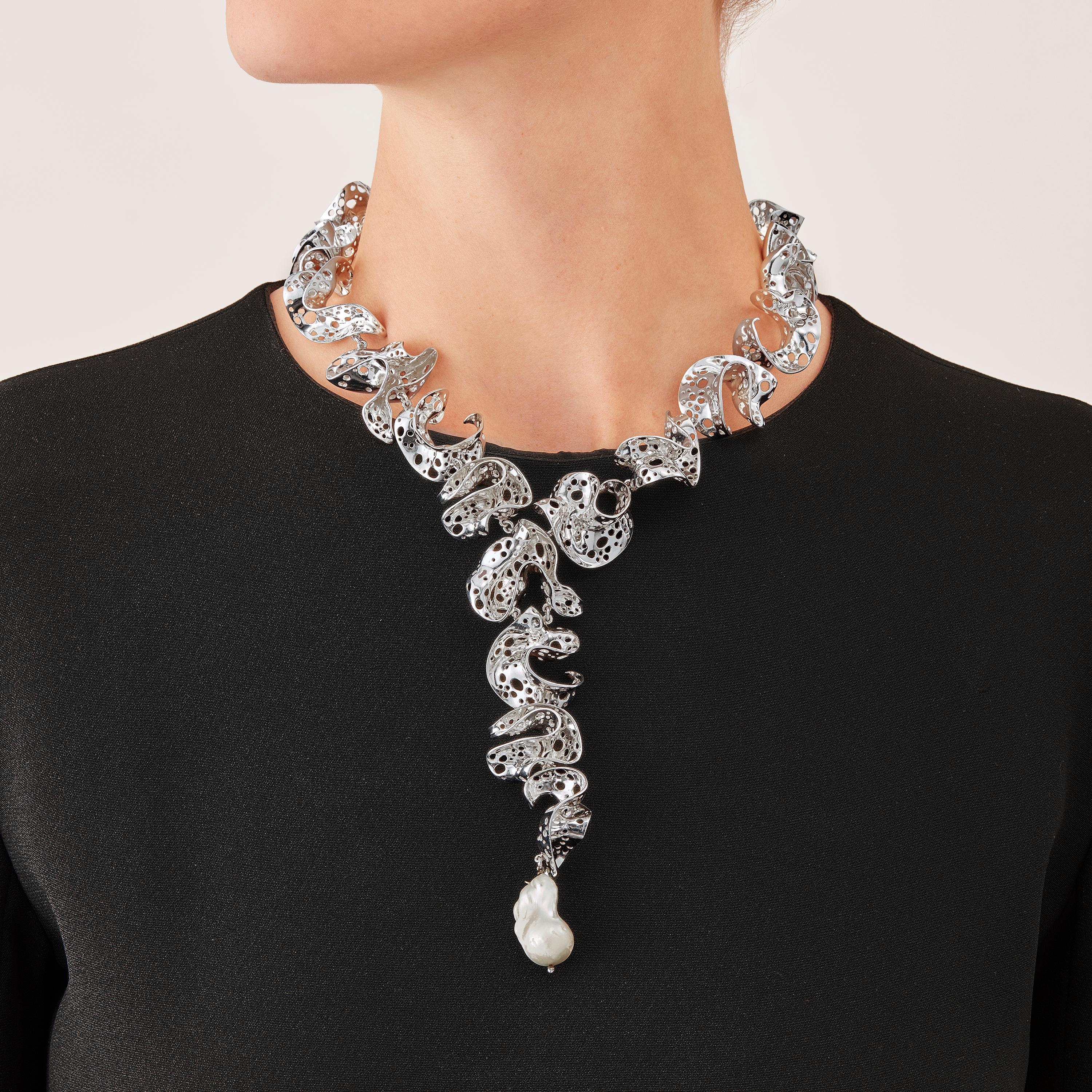 With their delicate, curved, free-form surfaces, the eighteen elements of this contemporary sculpture Necklace fold and unfold with harmony and grace like  glittering shell fragments or polished metalized leaves. Discreetly linked to one another