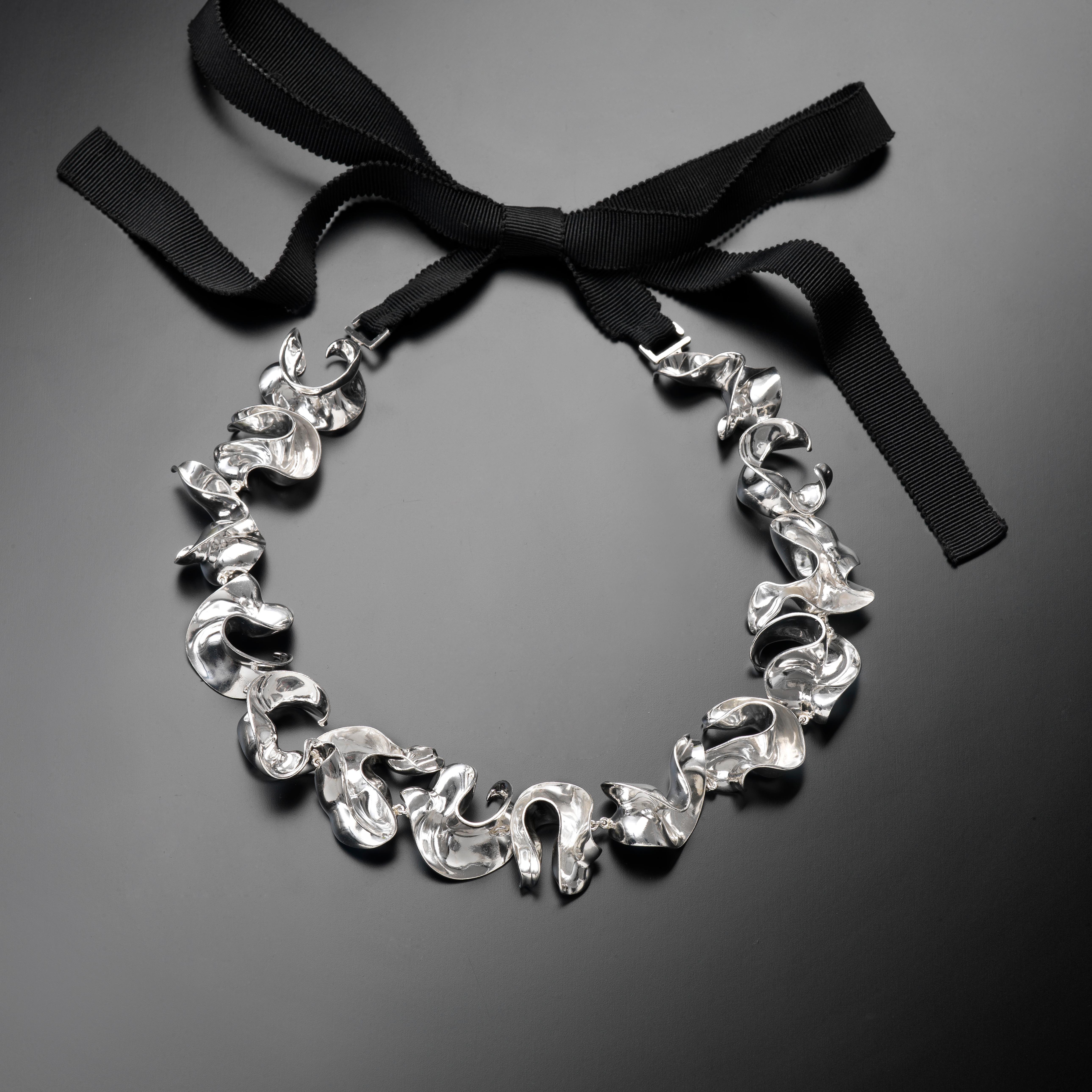 With their delicate, curved, free-form surfaces, the fourteen elements of this contemporary sculpture necklace fold and unfold with harmony and grace like glittering shell fragments or polished metalized leaves. Linked to each other with small