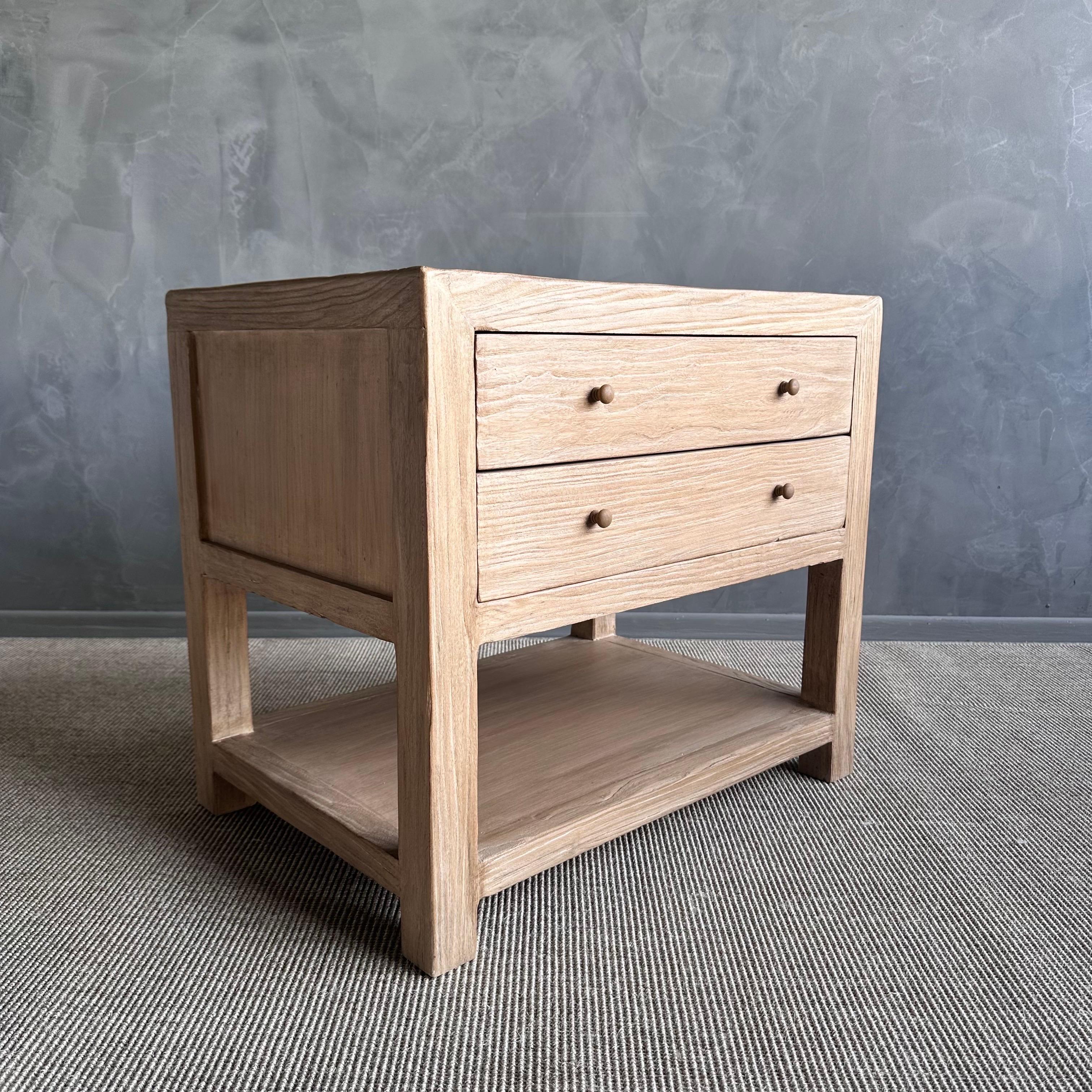 Presenting the Nathalie Nightstand, made from sturdy reclaimed elm wood with a lovely natural finish and wax coating. 
This nightstand includes two drawers and a shelf, providing plenty of storage space for your bedside necessities. Its wabi sabi
