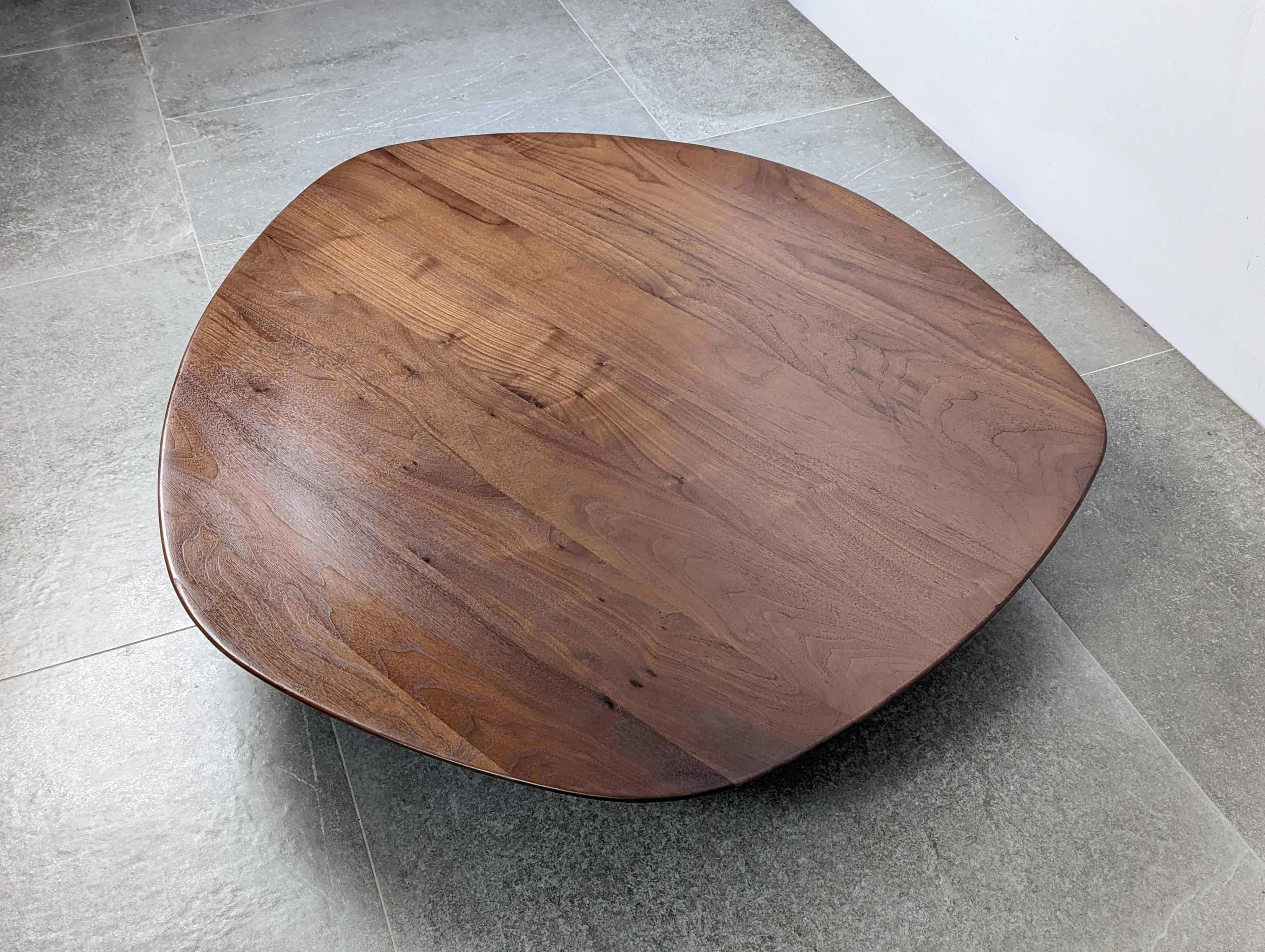 The Pebble table, designed by Nathan Young in 2008 for Ligne Roset, is a stunning example of modern design. His inspiration in the form of a stone carved by river water gives it a fluid and organic appearance. The solid, carved walnut top stands on