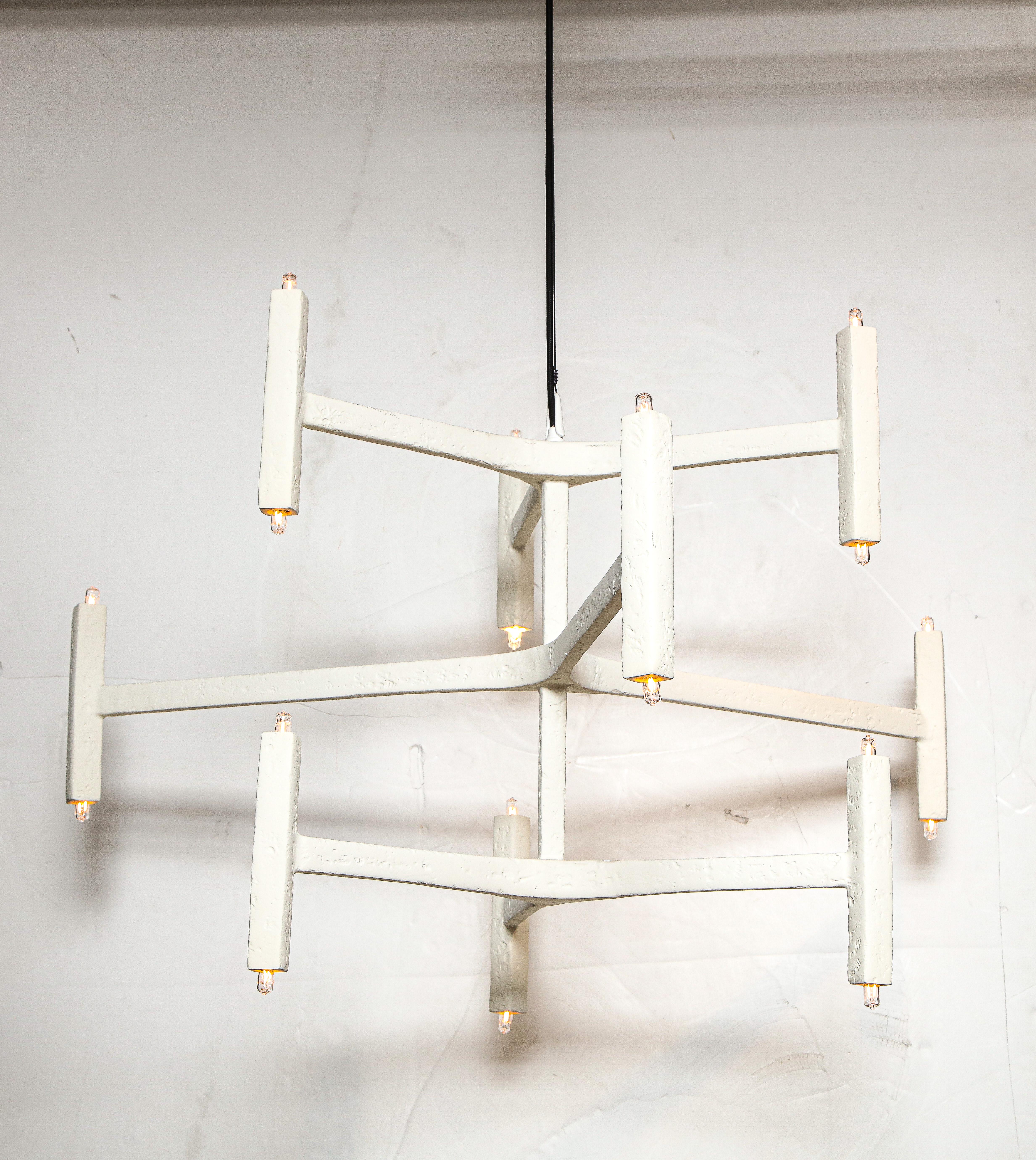 Questo lampadario a nove bracci con finitura in gesso è appeso a un cavo d'acciaio e sembra fluttuare nello spazio. Da ogni punto di vista, il design simmetrico cambia le prospettive. Per aggiungere un tocco di colore si utilizza un filo elettrico