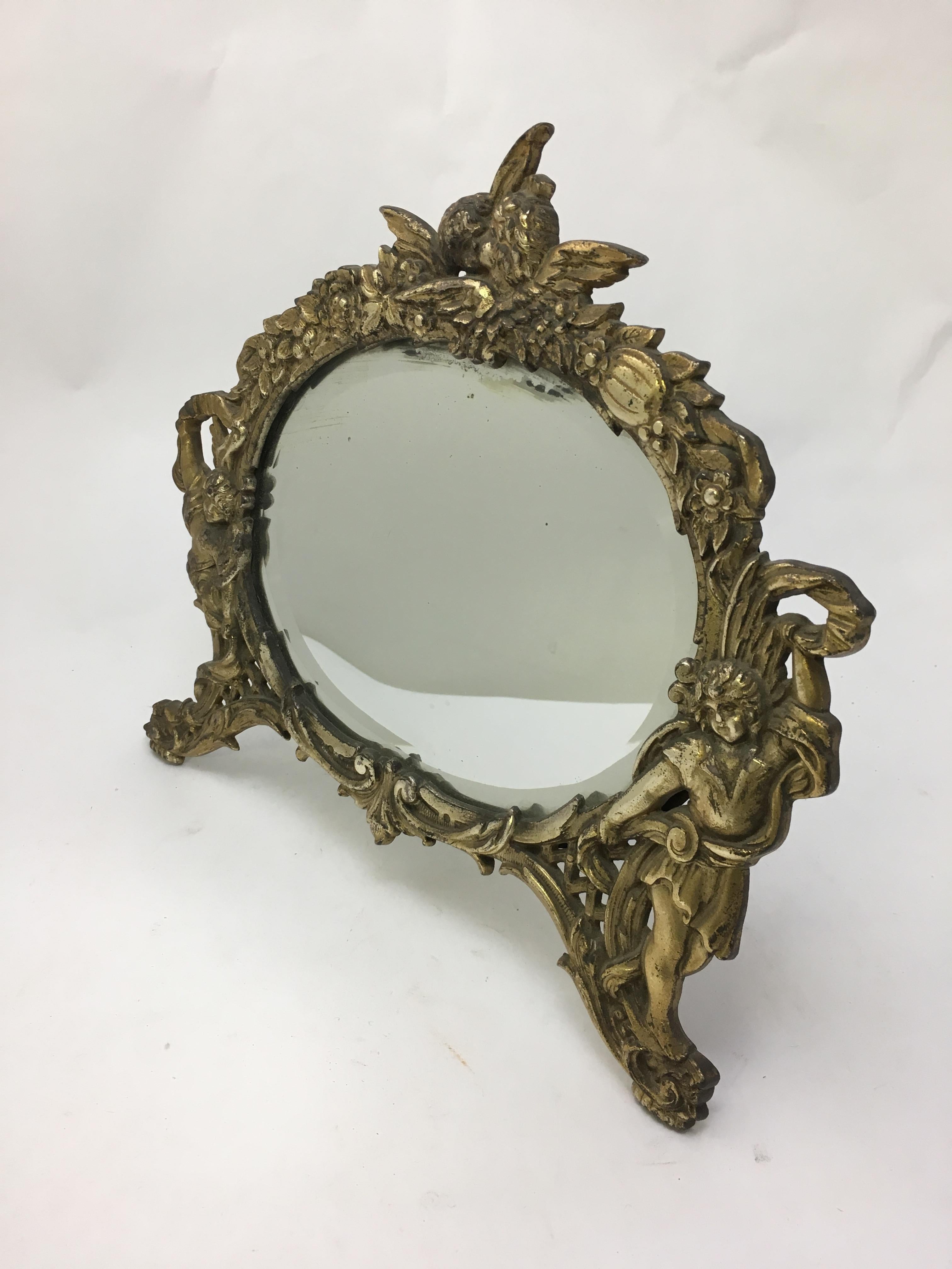Gilded cast iron standing mirror decorated with floral scroll and putti motif. Oval bevel glass mirror. Fully signed on reverse, NB&IW, 2000, circa 1910. 

Measures: 6