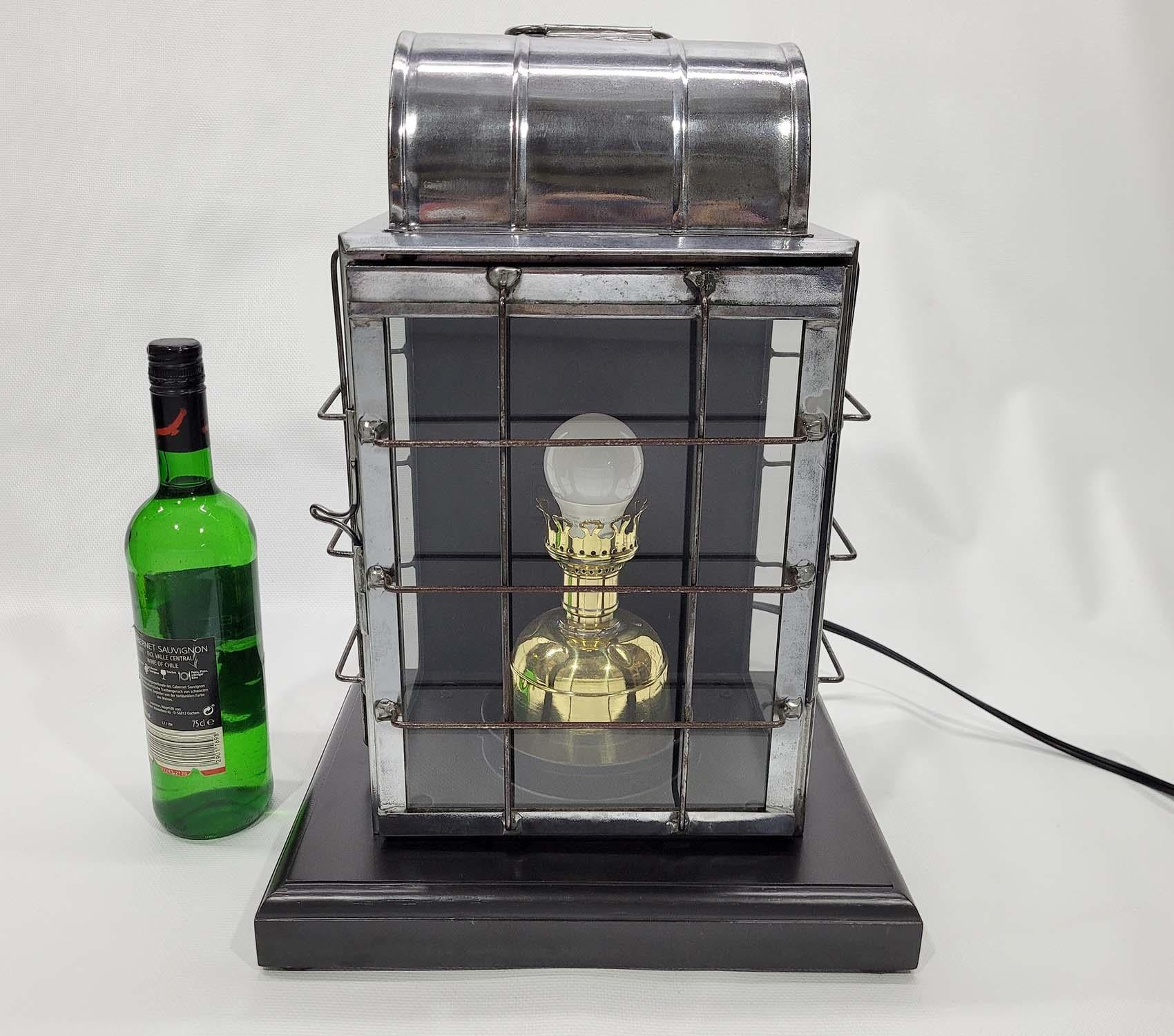 Ships lantern by the National Marine Lamp Company. Polished steel case with protective wire cage. The brass burner has been fitted with an electric socket. The lantern has been mounted to a custom-made wood base. Circa 1910

Weight: 13