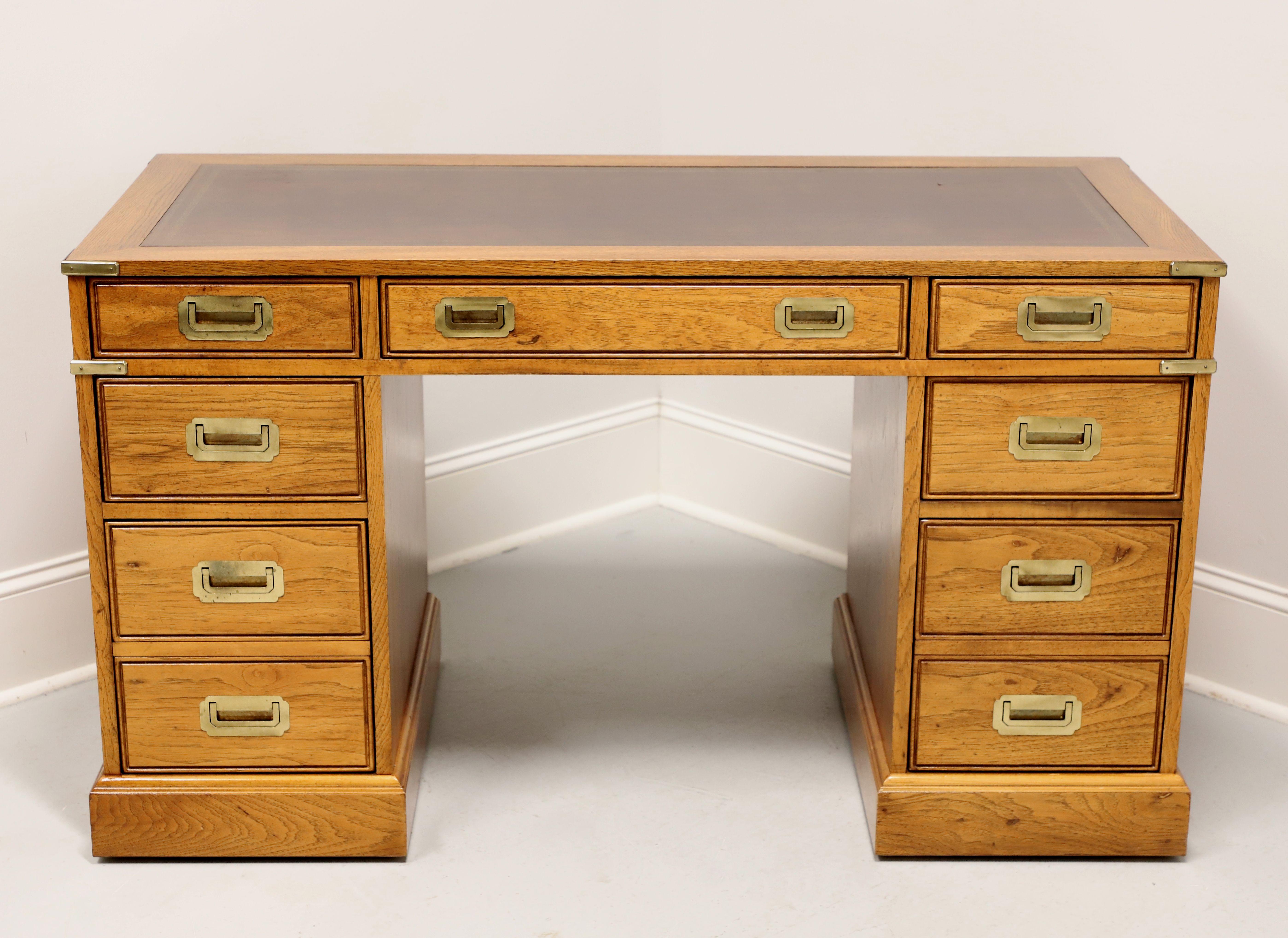 A Campaign style kneehole desk by National Mount Airy Furniture. Solid oak, embossed brown leather top, brass hardware & accents, and a solid base. The user side of the desk features seven drawers of dovetail construction, including a center drawer