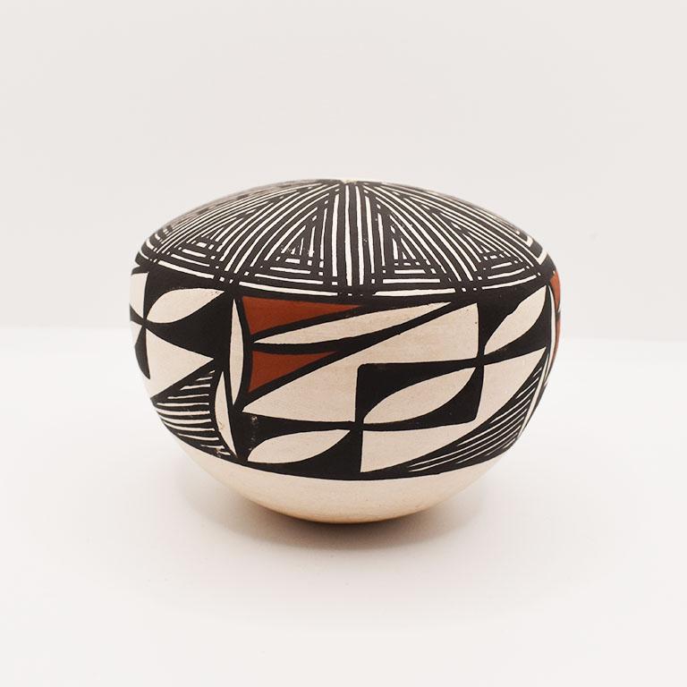 Ce pot de graines amérindien polychrome unique est de forme ronde et décoré d'un ensemble de formes géométriques avec un motif figuratif sur le dessus. Les couleurs sont le brun profond, le rouge-orange et la crème. Le sommet comporte un petit trou