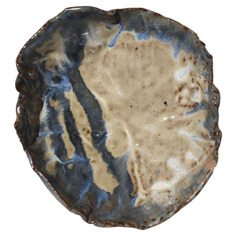 A one-of-a-kind hand-made ceramic trinket dish by Native American artist Clyde L. Otipoby. At first glance, this piece reminded us of an oyster. It is round with irregular edges. It is glazed in a mixture of blues, creams, and browns. It sits upon