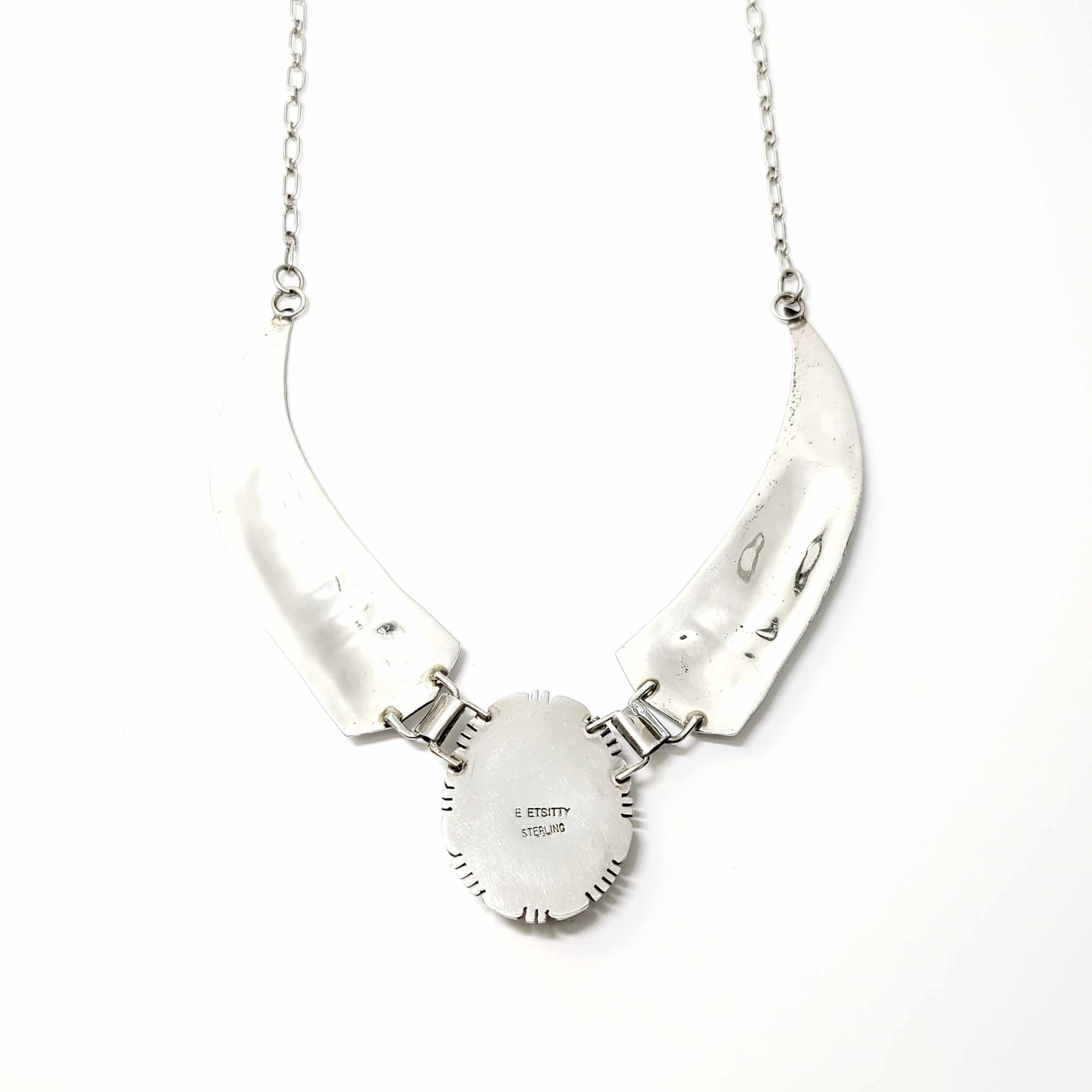 Halskette aus Sterlingsilber und braunem Türkis von der indianischen Kunsthandwerkerin E. Etsitty. 

Scharnierhalskette mit einem runden Anhänger in der Mitte mit einem großen ovalen braunen Türkis mit blauen Flecken in einer Seilfassung mit