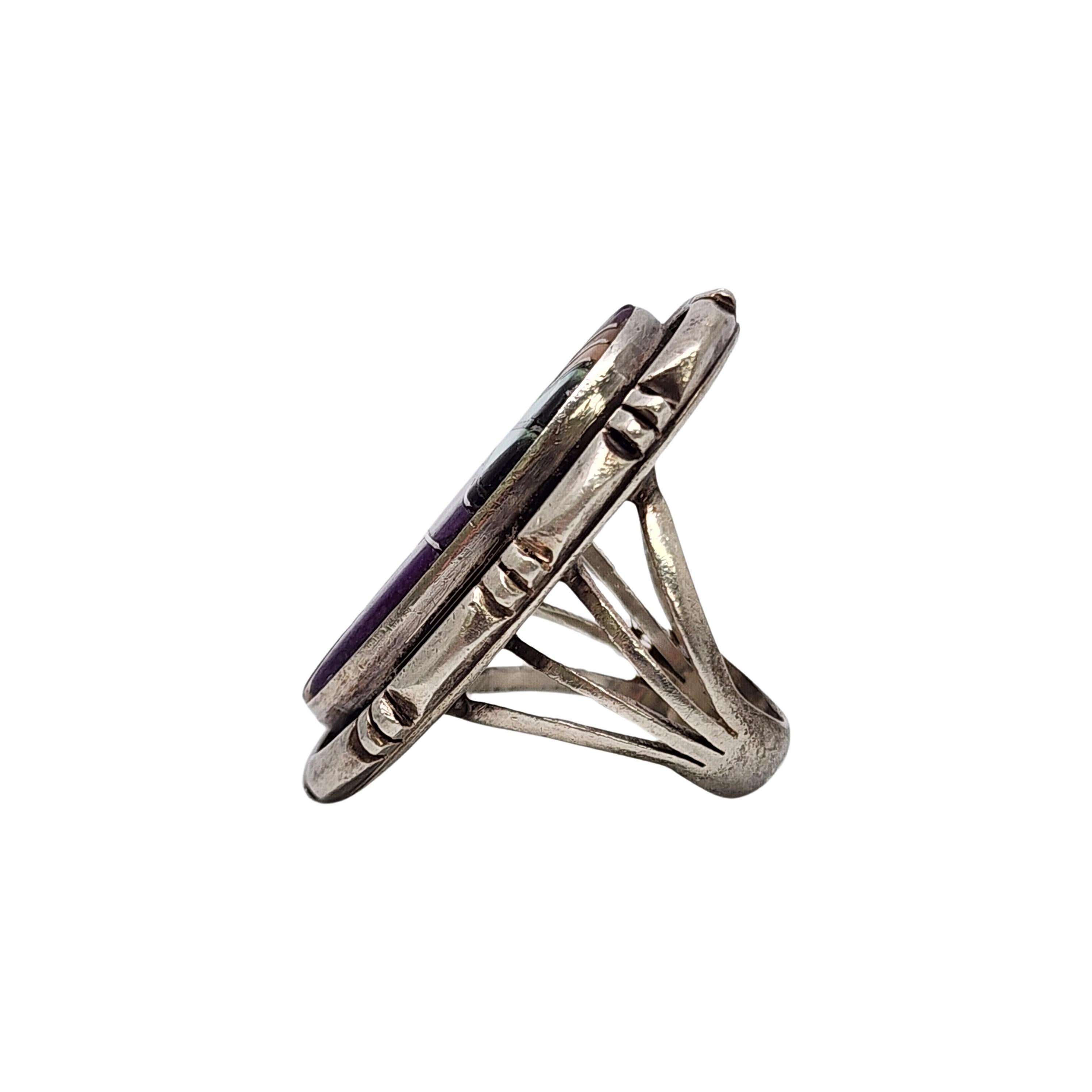 Anillo de plata de ley con incrustaciones de varias piedras, obra de la artesana nativa americana Evelyn Spencer.

Talla 6

Esta pieza presenta un gran diseño de incrustación oval, las piedras parecen ser nácar, sugilita, ónice y coral rosa. El
