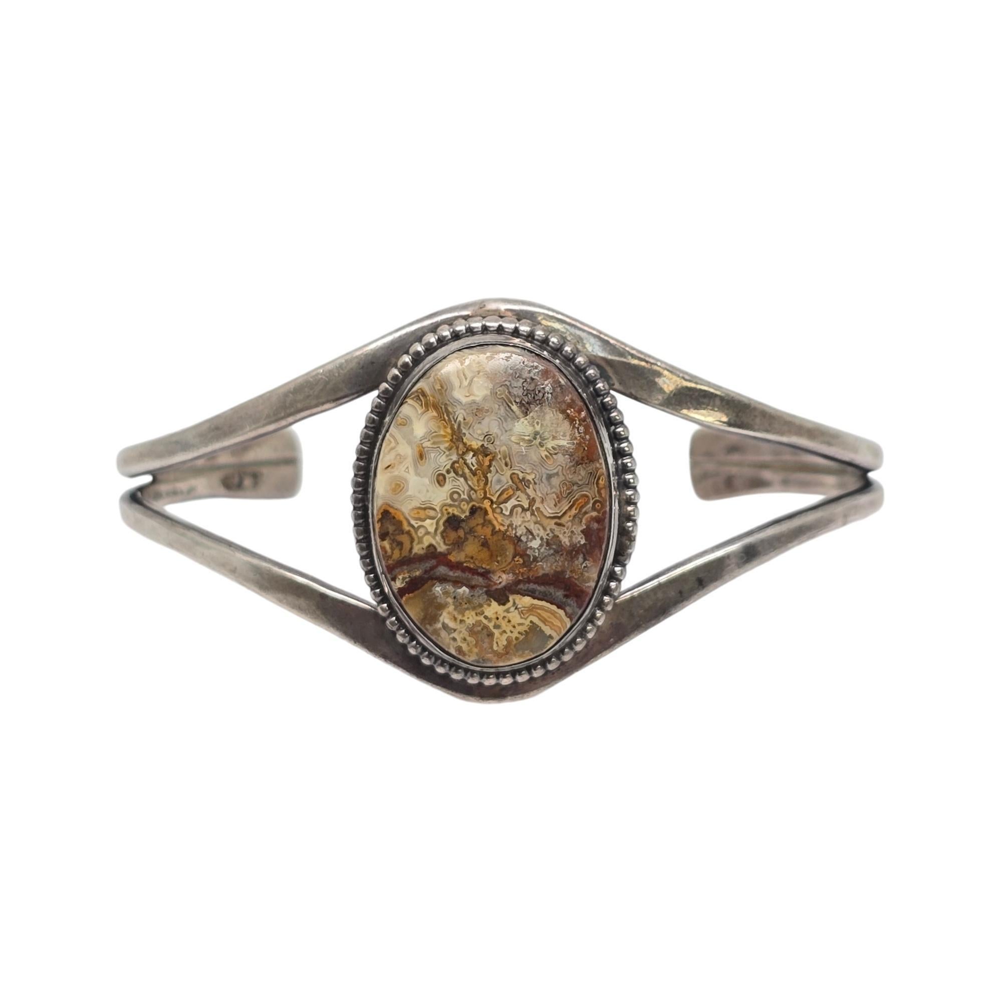 Pulsera brazalete de plata de ley y ágata de encaje del artesano nativo americano hopi Floyd Namingha Lomakuyvaya.

Esta pulsera presenta una hermosa ágata de encaje grande, ovalada y veteada de color marrón, engastada en bisel con un marco de
