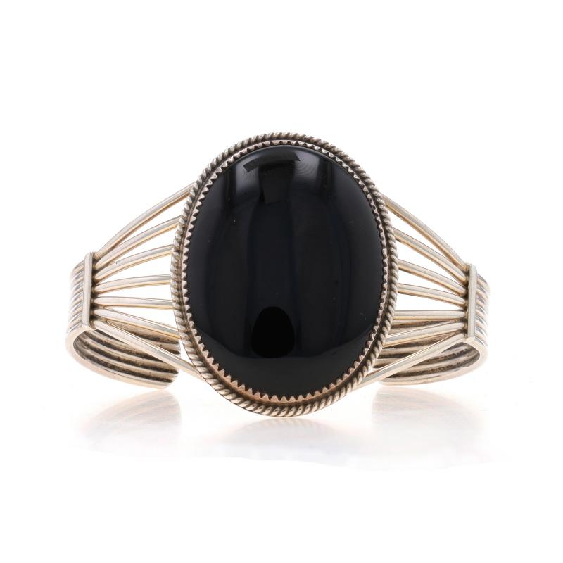 Native American
Tribal Affiliation: Navajo

Metal Content: Sterling Silver

Stone Information
Natural Onyx
Cut: Oval Cabochon
Color: Black

Style: Solitaire Cuff
Fastening Type: N/A (slides over wrist)
Features: Open Cut Detailing & Rope