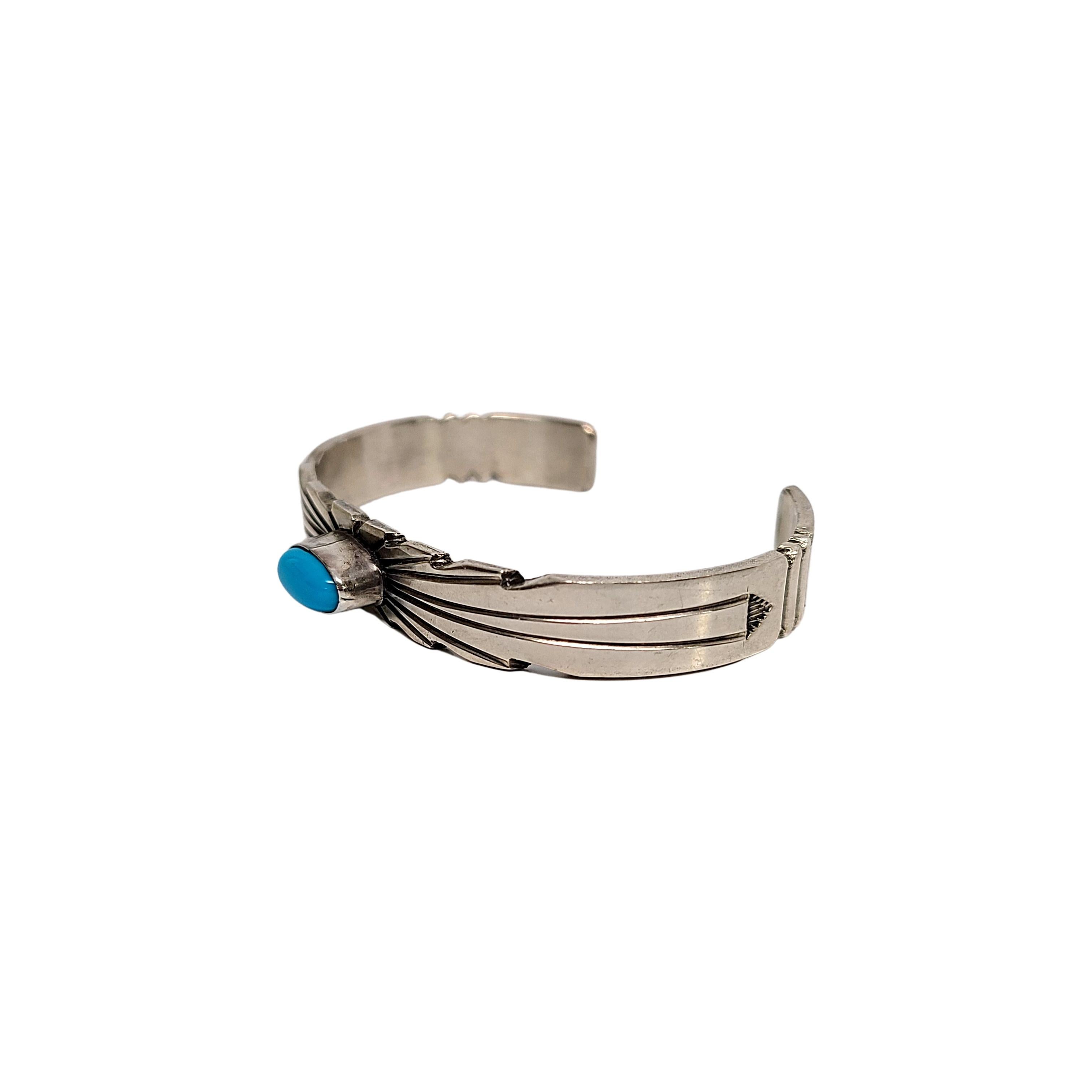 Sterling silver and turquoise cuff bracelet by Native American artisan, Ray Bennett.

Bezel set oval turquoise in the middle of a traditional starburst design with stamped arrow accents at ends.

Measures approx 5 1/4