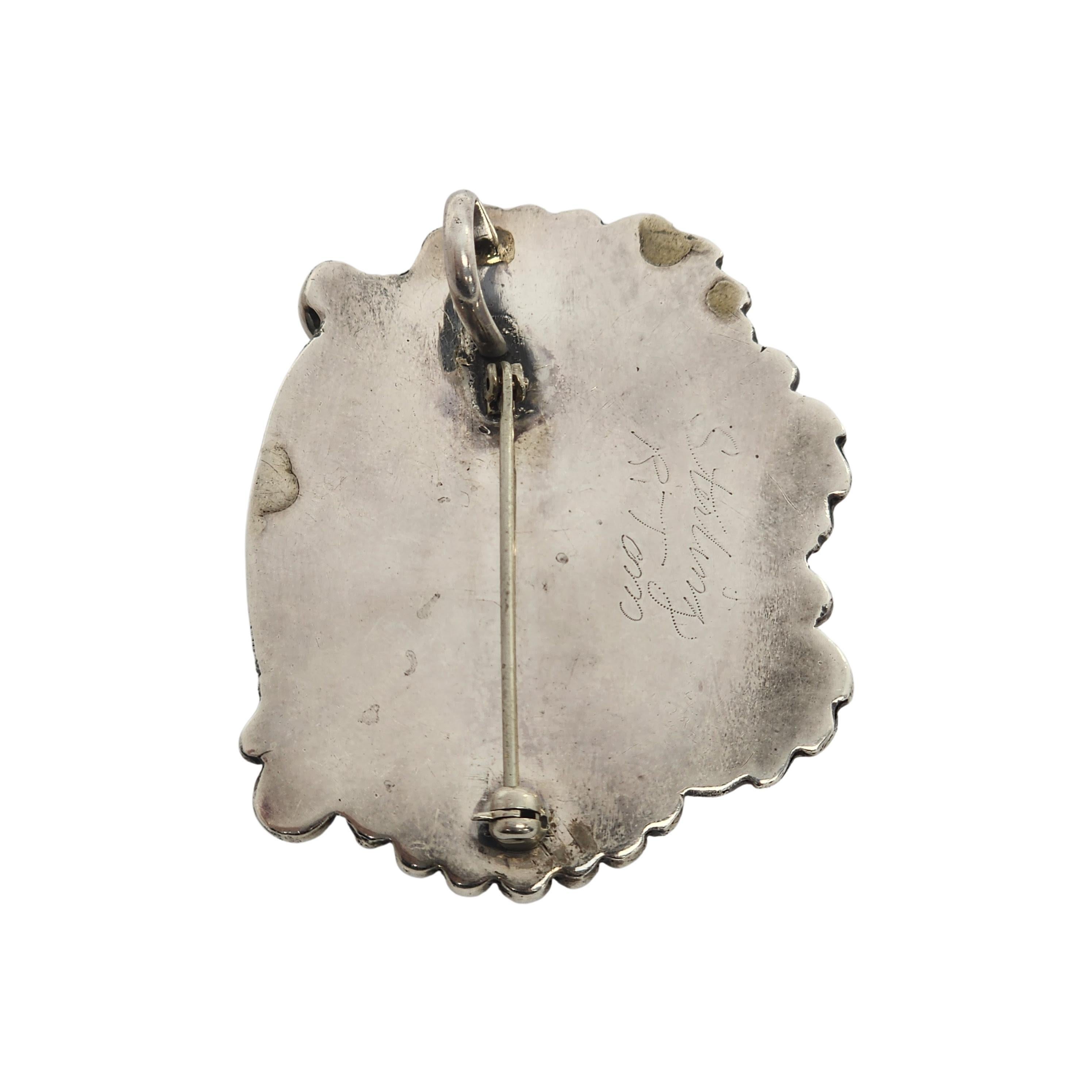 Ciondolo/spilla in argento sterling e piume di onice dell'artigiano nativo americano Navajo Ronald Tom.

Il grande onice nero ovale è inserito in un castone a dente di sega circondato da piume e perline. Può essere indossato come ciondolo o