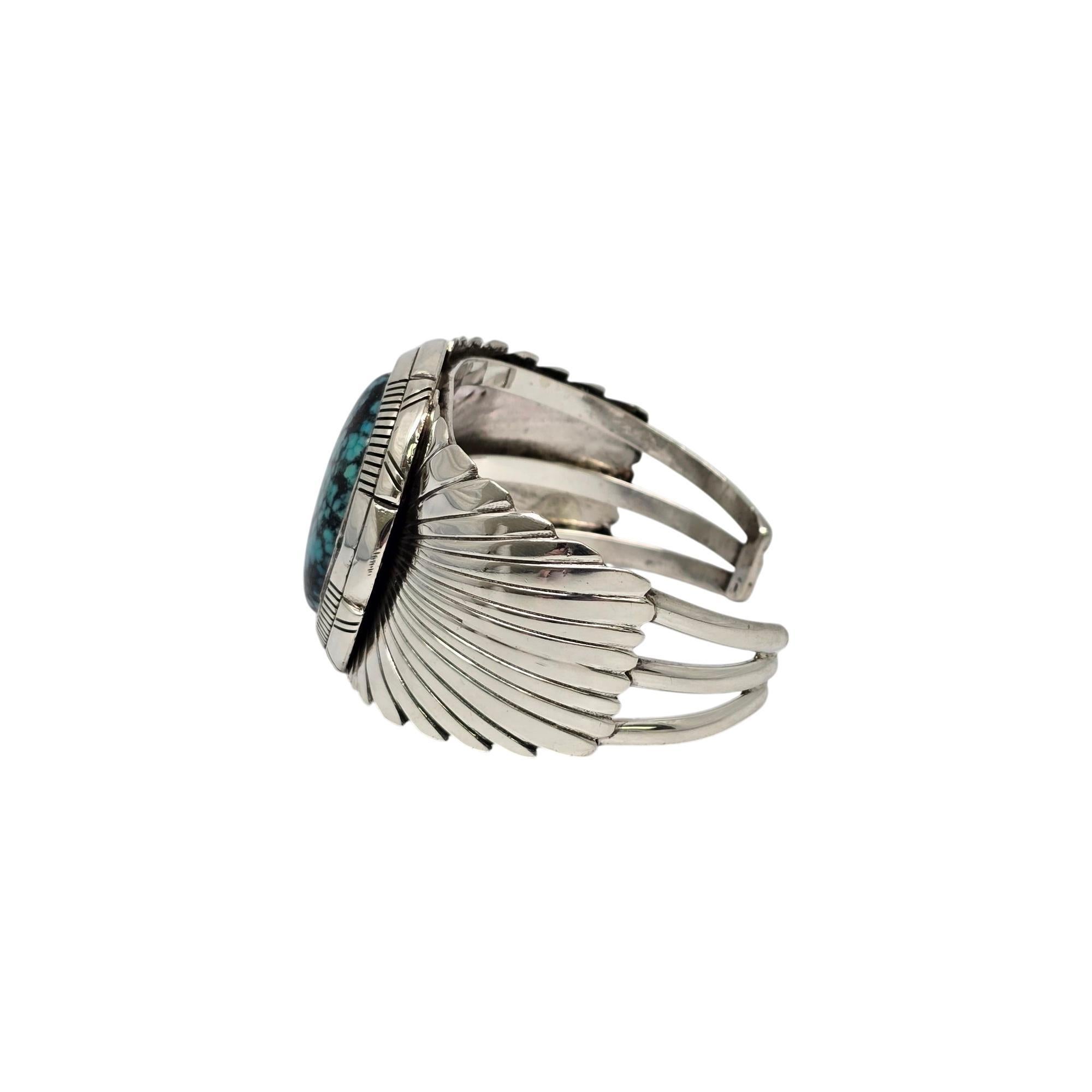 Sterling silver and turquoise wide cuff bracelet by Native American artisan, signed DD.

A beautiful, large oval shaped turquoise stone is bezel set in a double hand carved bezel with applied wing-like shoulders. There is a dent on one shoulder (see