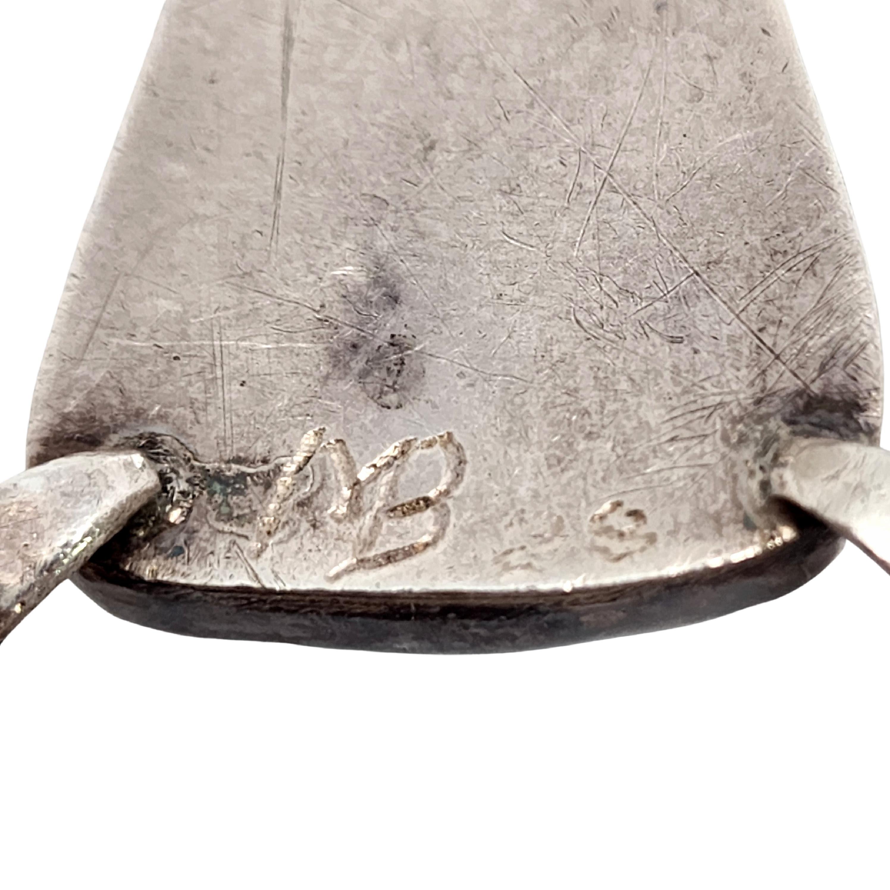 Collana con ciondolo in argento e turchese di un artigiano nativo americano, firmata MB.

Firmata con una MB incisa, questa sostanziosa collana presenta diversi tipi di perline d'argento e un grande ciondolo a triangolo con lavorazione a giorno e