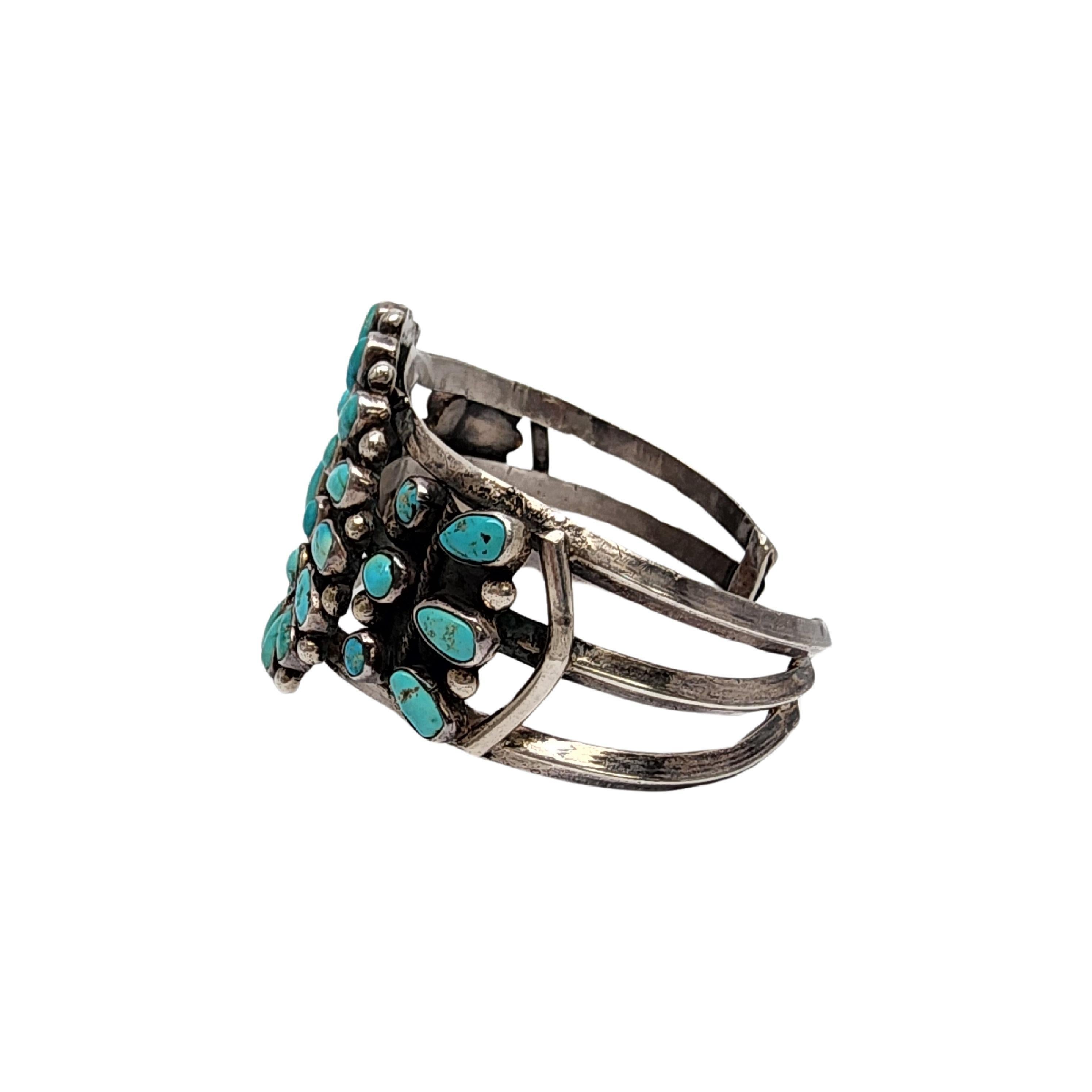 Silver turquoise cluster cuff bracelet by Native American artisan.

This large and substantial piece is a beautiful example of Grandmother cluster design featuring blue turquoise stones with rope accents.

Weighs approx 61.1g, 39.3dwt

Measures