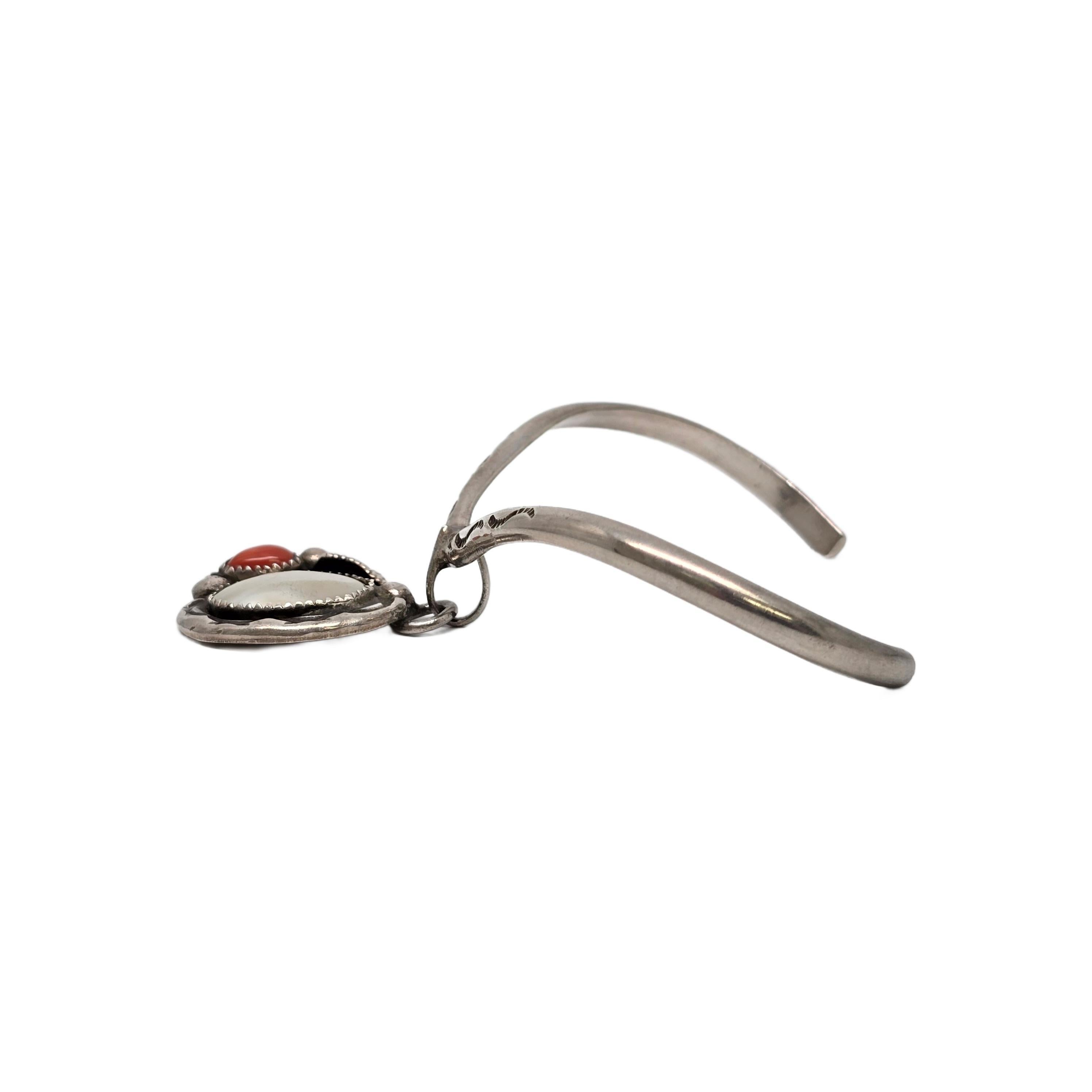 Bracciale a V in argento sterling con pendente realizzato da un artigiano nativo americano Navajo.

Un bracciale sottile con accento stampato a forma di V è caratterizzato da un pendente con madreperla e corallo in castoni a dente di sega, accenti
