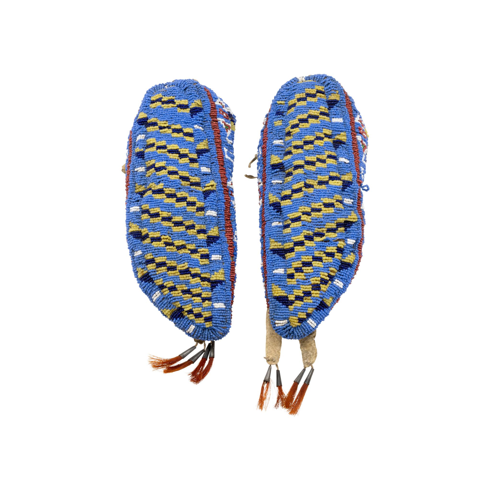 Native American Sioux Indian fully beaded hide moccasins. Sinew sewn and beaded using colors of medium blue, red white heart, greasy yellow, cobalt, white and brass. Forked tongues and tin cones with red horsehair. Exquisitely made pair in nice