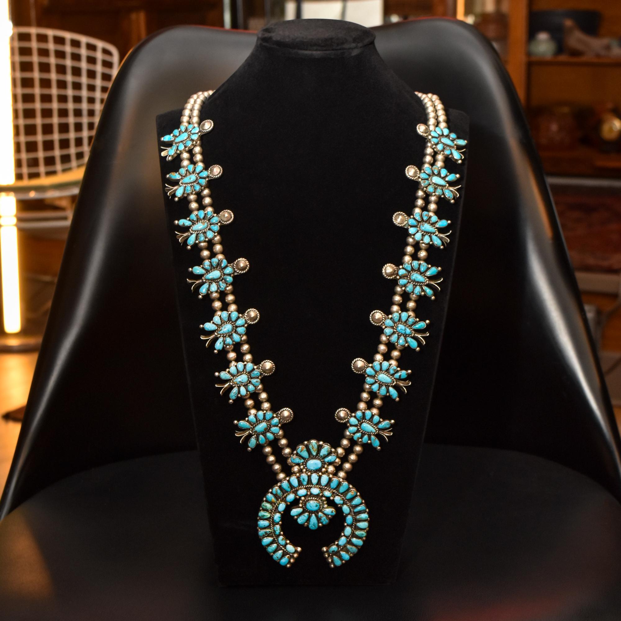 A gorgeous Native American squash blossom necklace with over 190 natural turquoise stones. This beautiful necklace is made from sterling silver and features 14 traditional squash blossoms, a robust Naja pendant, and handmade silver bench beads. The