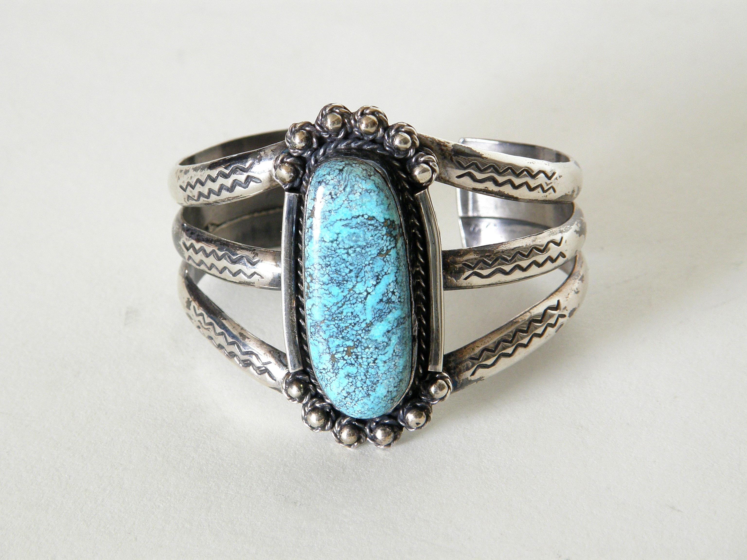This Native American sterling cuff bracelet features a lovely, light blue turquoise stone with a fine, dark matrix that has some scattered, coppery highlights. It has an irregular, elongated oval shape, and the thick stone sits high in its bezel