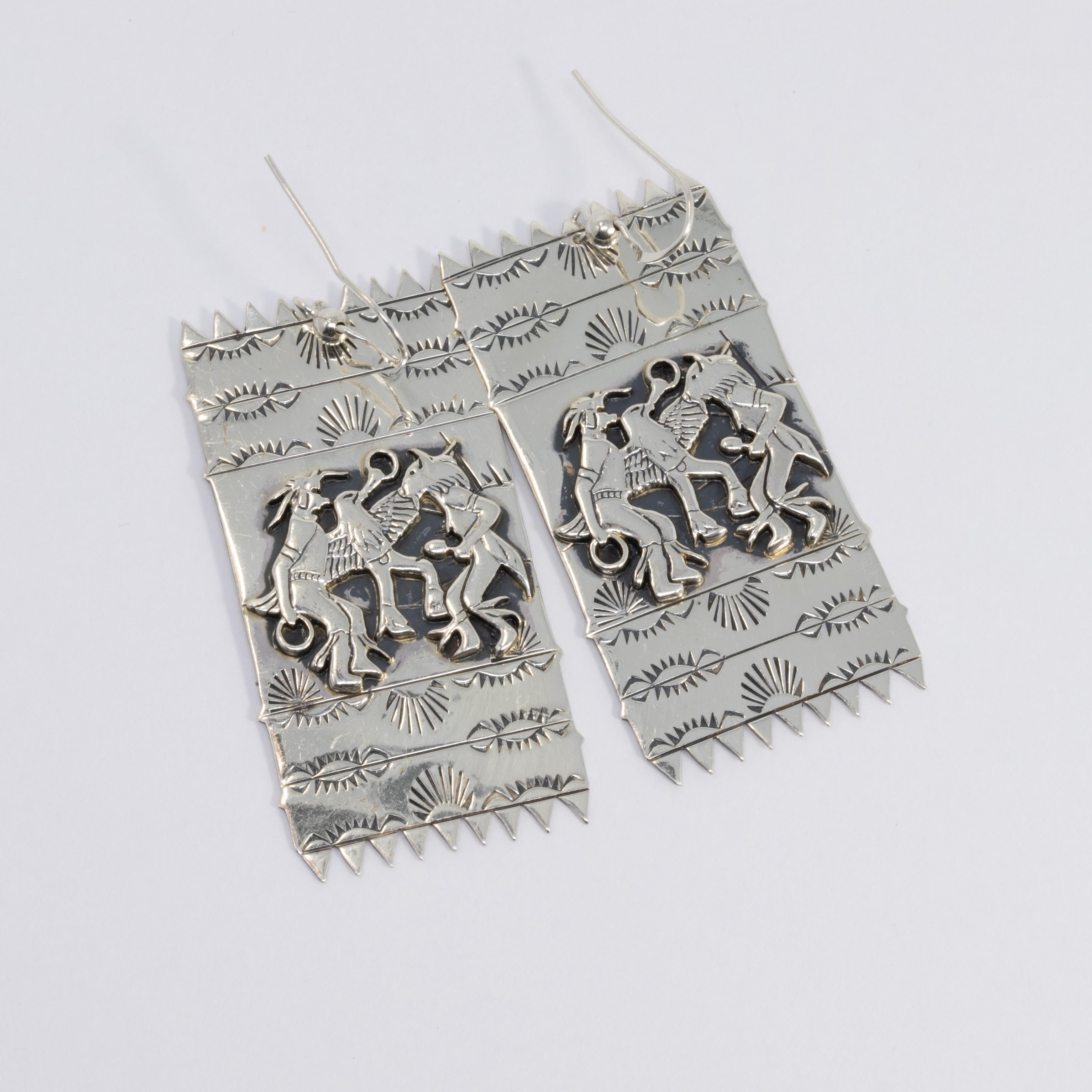 A pair of finely detailed sterling silver earrings, depicting three dancing Native American deities. Rectangular shape with polished sawtooth ends.

Hallmarks: STER © SC