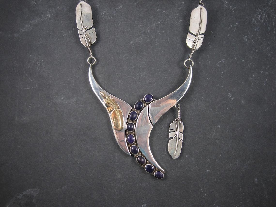This huge, amazing necklace is a one of a kind creation by Navajo silversmiths Wilbert and Cora Vandever.

Its sterling silver with a 14k yellow gold feather and 10 beautiful sugilite gemstones.

The focal measures 3 3/4 by 5 inches.
End to end,