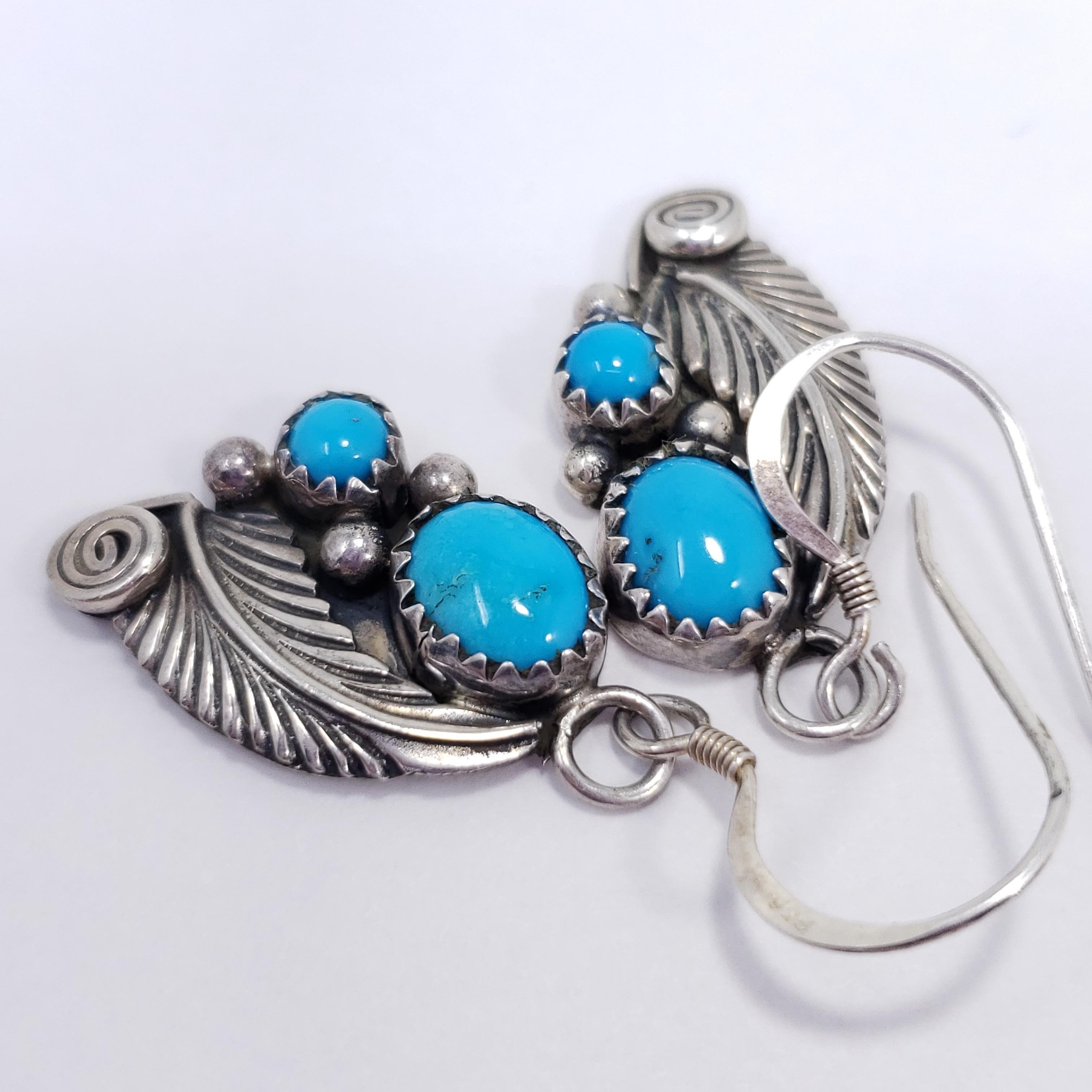 A pair of handmade Native American feather-themed earrings, each featuring a pair of vibrant turquoise cabochons in a sterling silver setting. 

Circa late 20th century. 

Marks / hallmarks / etc:  Sterling, H