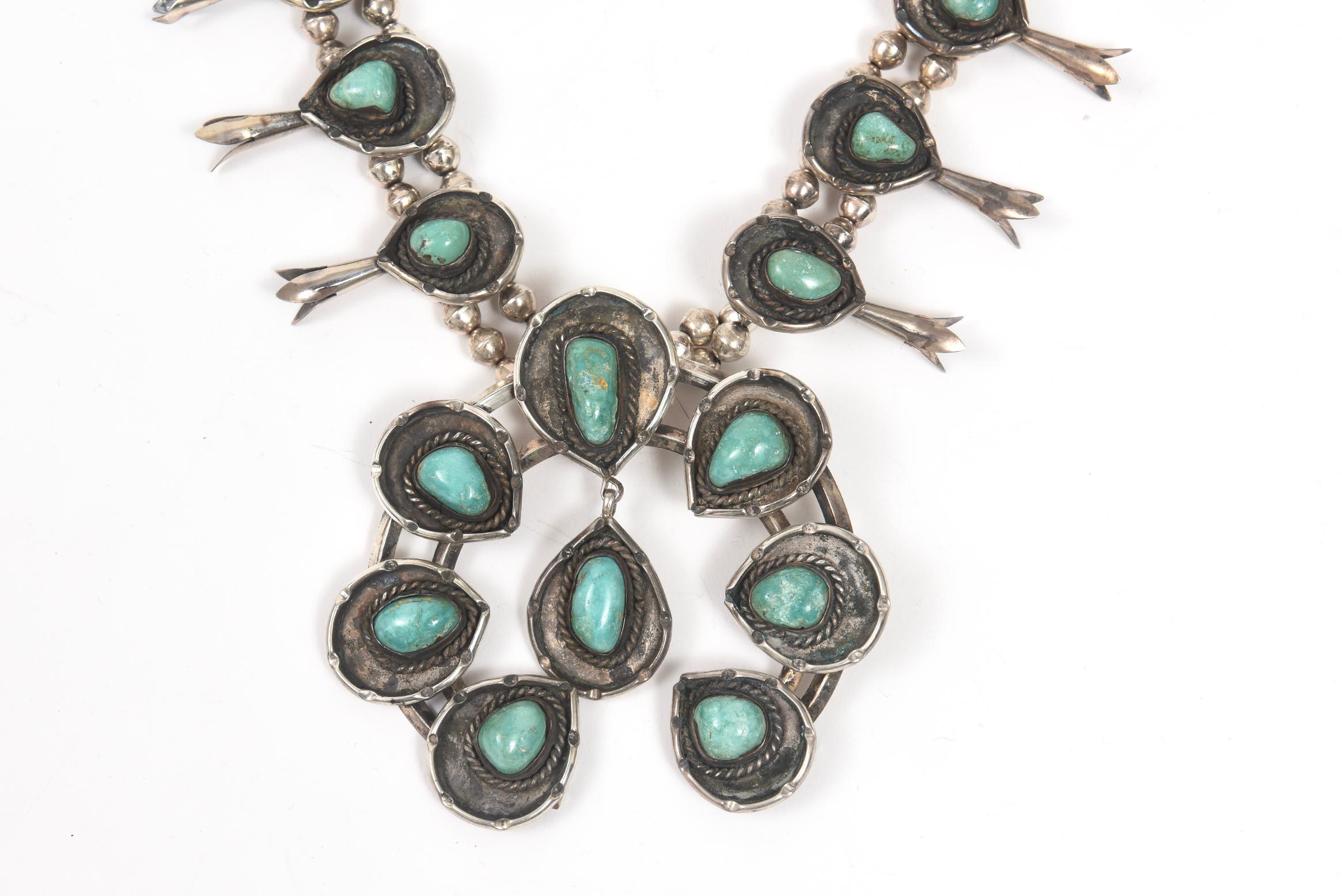 Vintage 1970s Navajo squash blossom necklace featuring blue-green turquoise stones combine with intricate sterling silverwork. The naja of the piece features eight turquoise stones in a teardrop frames,  A single teardrop piece hangs from the bottom