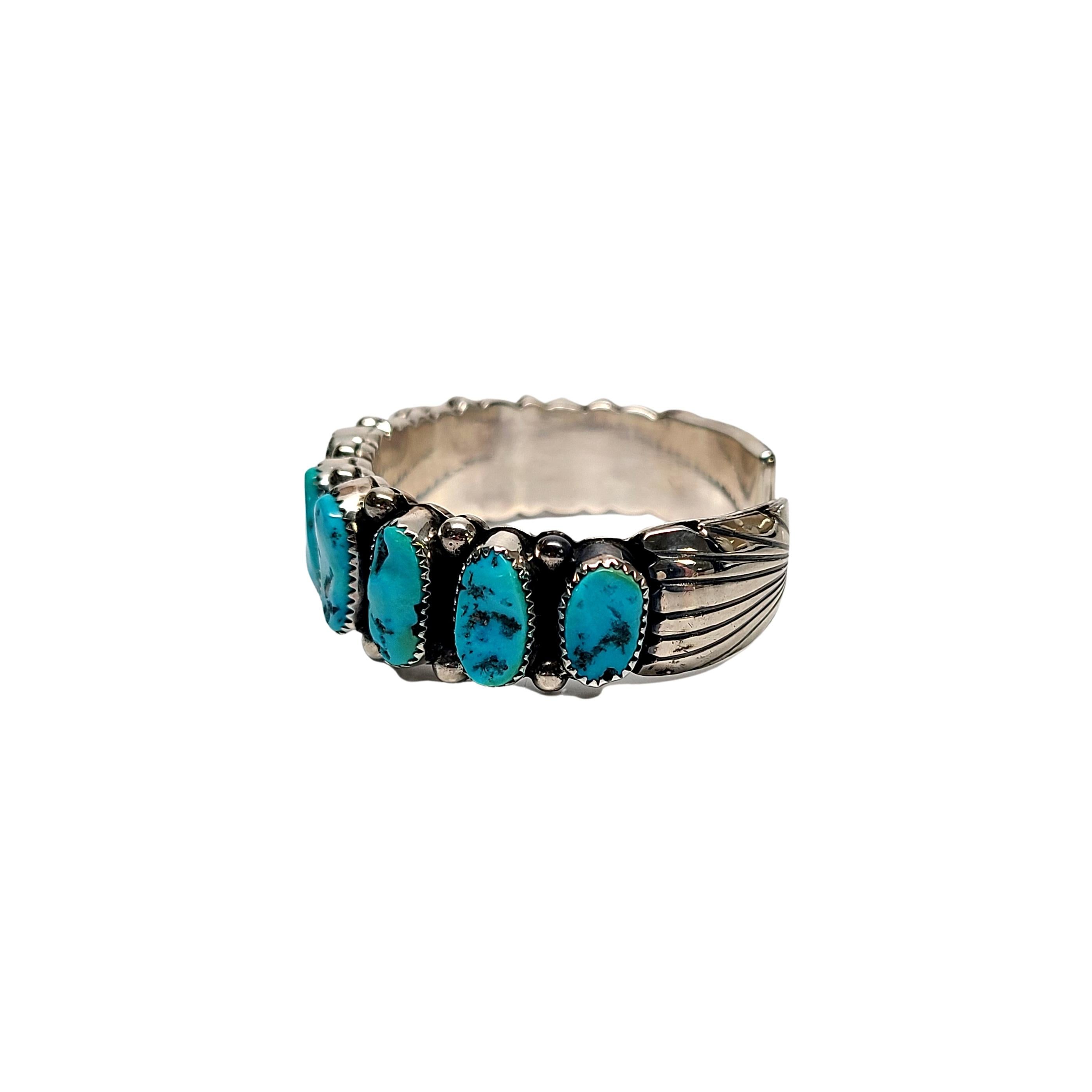 Sterling silver and turquoise cuff bracelet by Native American artisan Wilbur Musket.

Created by a Native American artisan Wilbur Musket, this piece features a row of turquoise stones in a saw tooth bezel setting with silver bead accents and