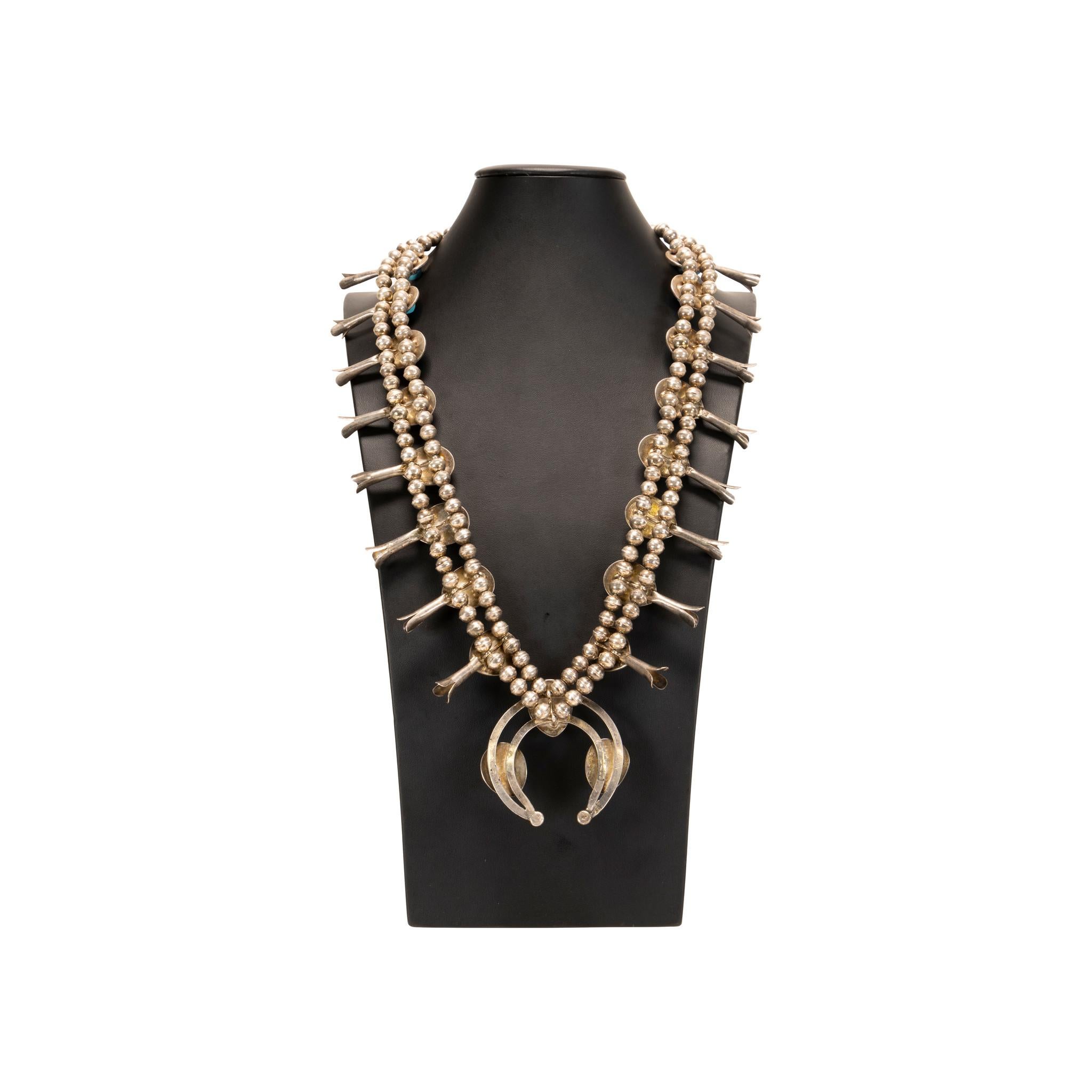 Collar de turquesa nativa de Kingman y flor de calabaza de plata de ley con 16 piedras excepcionales engastadas en un diseño de caja de sombra que termina en una naja adicional de tres piedras moldeadas en arena. Las piedras son de un azul claro