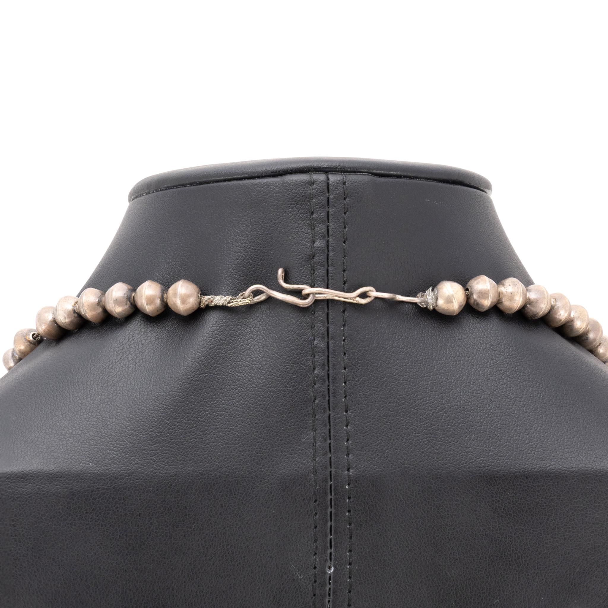 Native squash blossom turquoise and sterling silver necklace. Ten Kingman turquoise stones on double Navajo pearl chain, each stone set in scalloped shadowbox with twisted rope border and feather details. Two-stone naja with mirrored decorations.