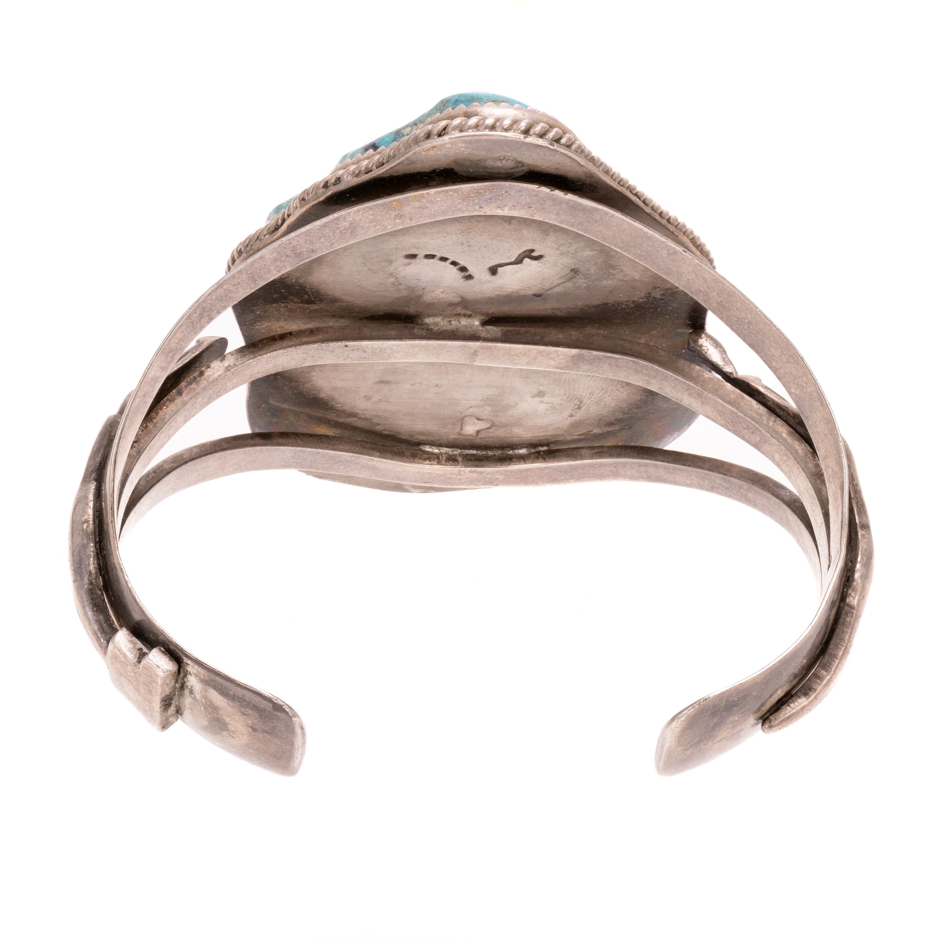 Bracciale in turchese Fox e argento sterling. Con una grande lastra di turchese naturale circondata da un bordo in corda ritorta e incorniciata da un bracciale aperto in sterling con figure femminili su entrambi i lati. Il turchese è di un blu