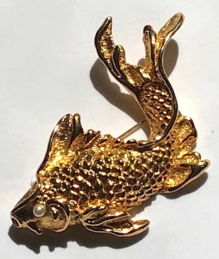 A beautifully cast gold fish brooch by Natori from the 1980s. Scales and fins are carefully detailed and executed on the fish in a downward swimming position. The eye has a faux pearl. Bright and shiny gold plate in excellent condition. The brooch