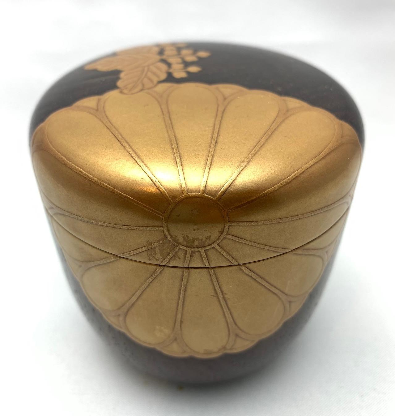 Natsume makie caddy container with chrysanthemum and paulownia motif. PreWar early Showa (1900 - 1939). Made from laquered wood with gold accents. Complete with original carrying sachet and box. Measures 7.5cm high and 7cm in diameter. Weights