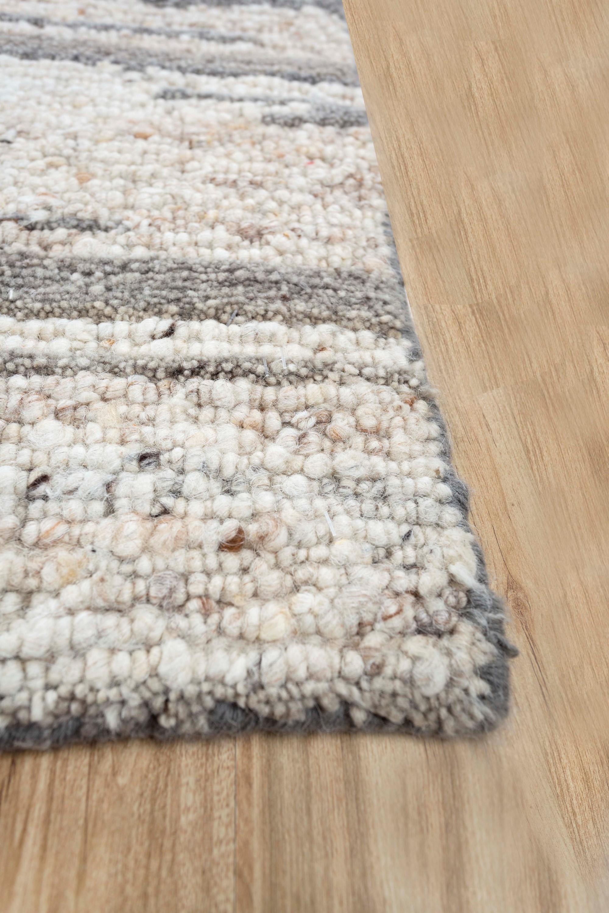 Our Uvenuti collection features this rug displaying an intriguing drift pattern that offers a sense of movement and tranquility, reminiscent of windswept landscapes. The rug's color palette is a harmonious fusion of medium taupe and natural white,