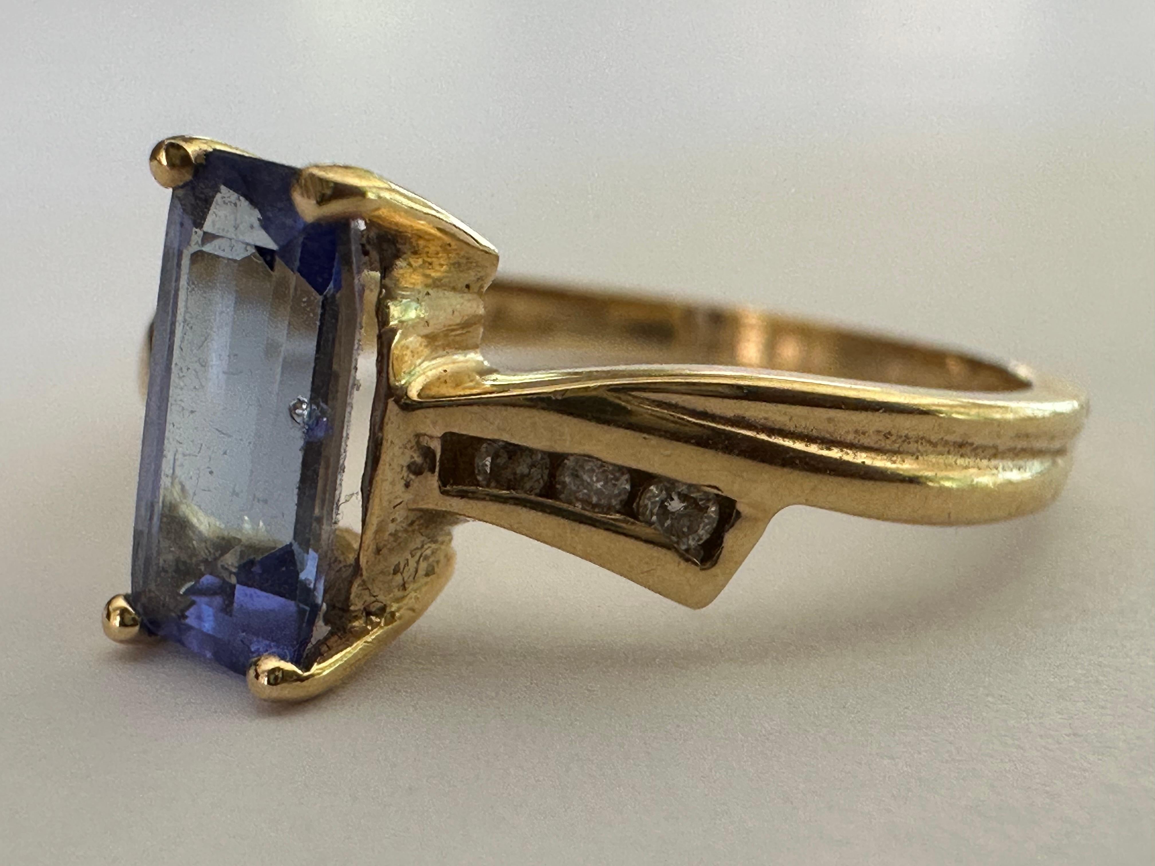 A natural light blue elongated cushion-cut tanzanite measuring approximately 1.28 carats centers this mid-century ring embellished with six small round diamonds, three on each side, in a bow design. Set in 14K yellow gold.  

