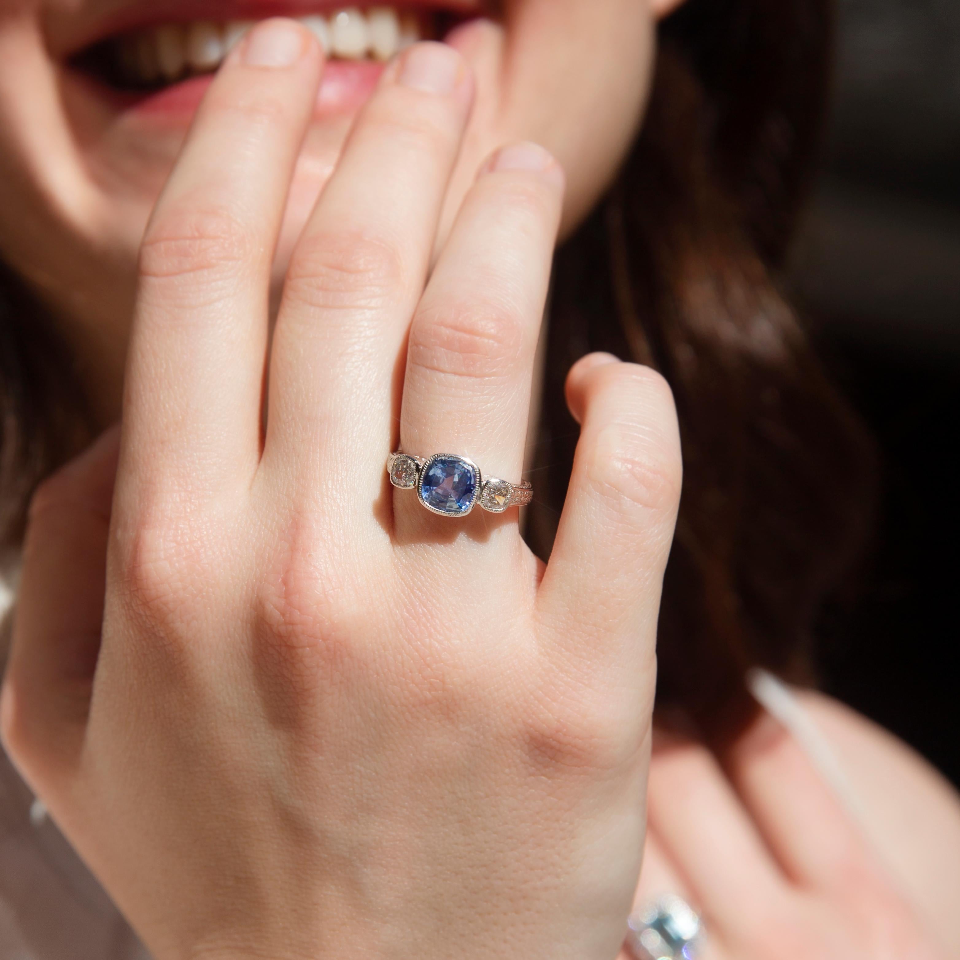 Forged with care in shimmering platinum, this fabulous three stone milgrain ring holds a gorgeous cushion-shaped blue sapphire flanked by a perfect duo of cushion cut diamonds glistening in unison. Her name is The Persida Ring. The harmony of