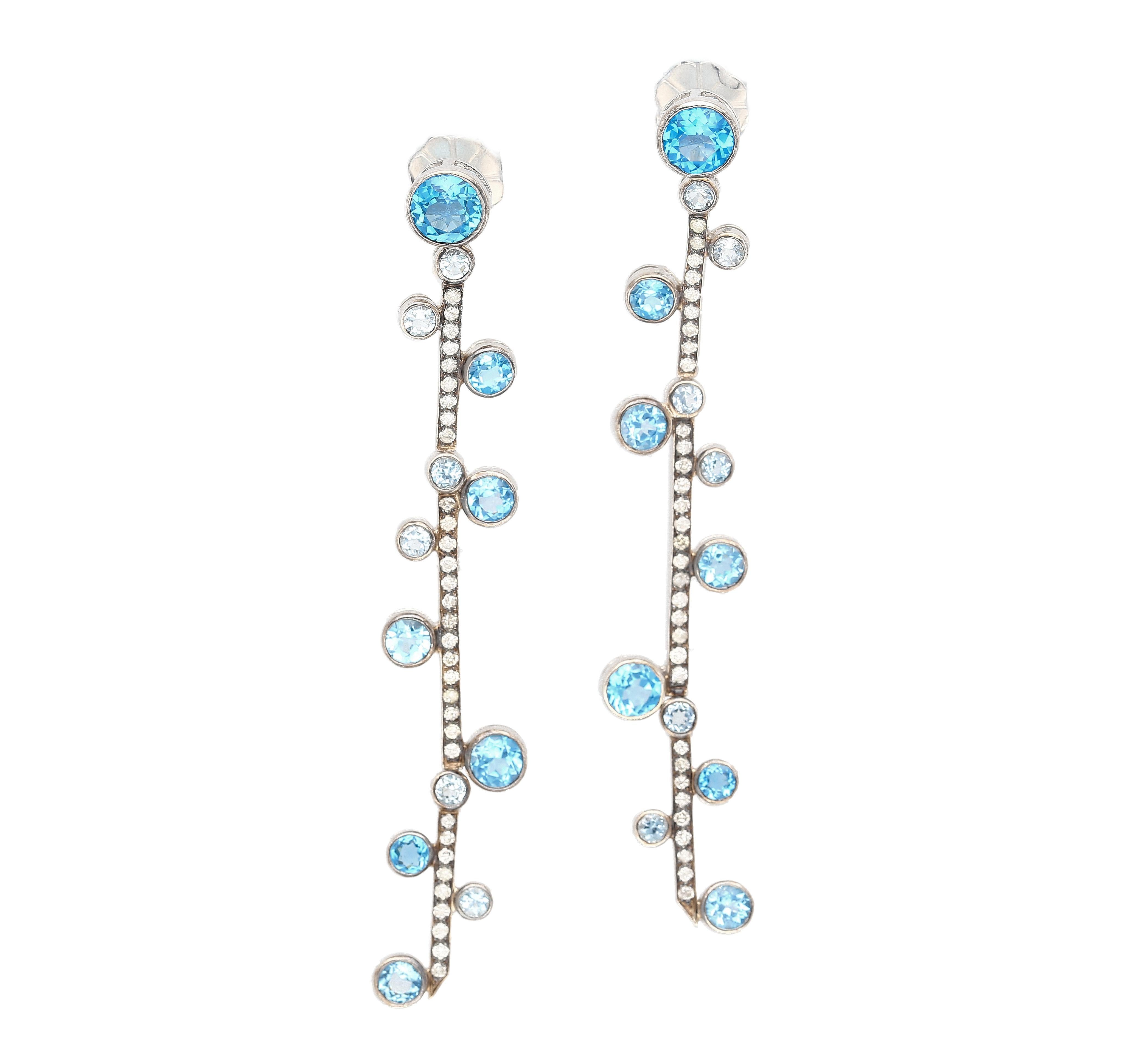 Natural Blue Topaz & Diamond Dangle Drop Earring in 18K White Gold. 

These dangle drop earrings feature 24 bezel-set natural blue Topaz gemstones, weighing 5.65 carats-total. The topaz is paired with additional round-cut diamond detailing, totaling