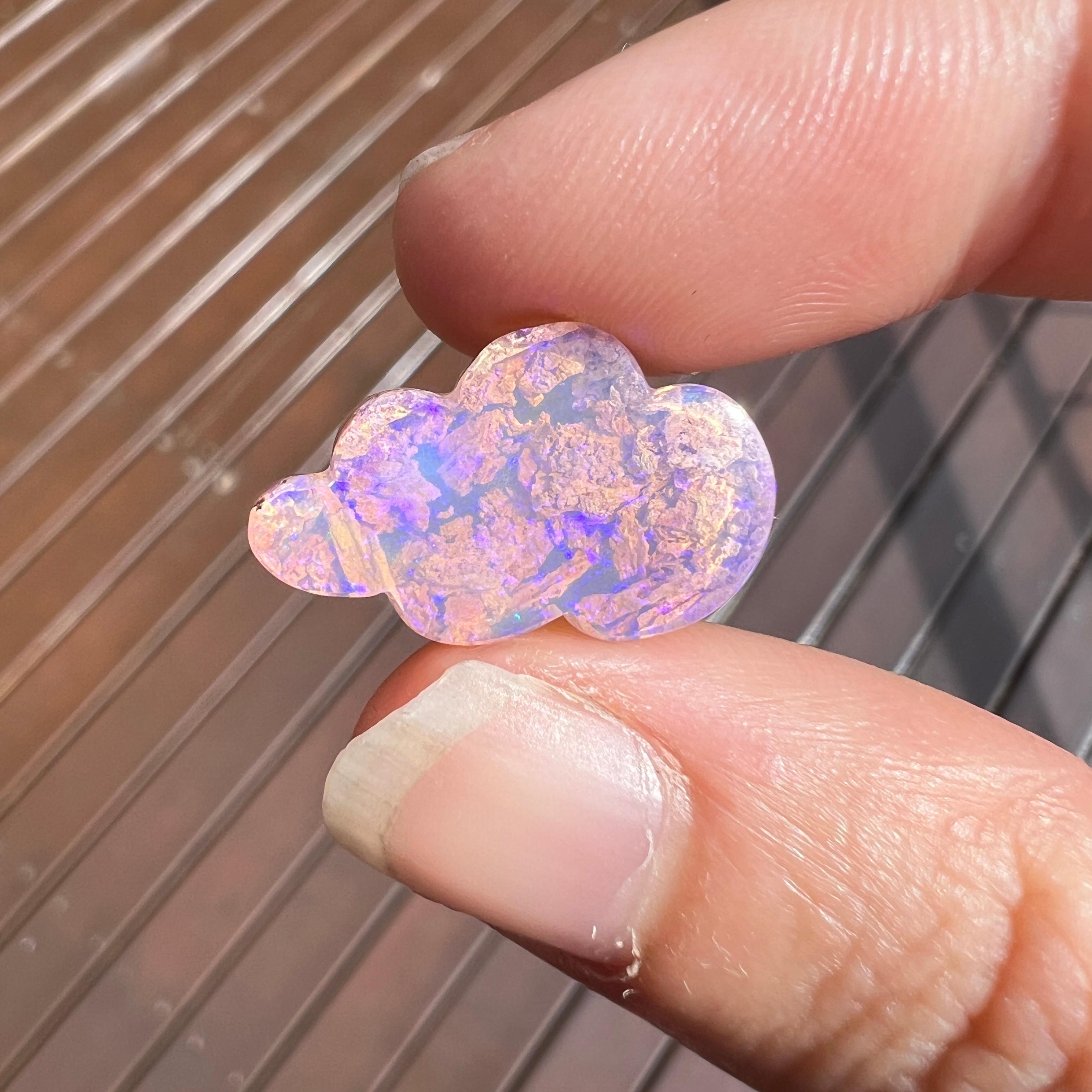 This brilliant purple 4.95 Ct wood replacement opal, carved into a cloud, is a truly exceptional addition to any collection, mined by Sue Cooper herself. Its rarity, coupled with its modern form, captivates connoisseurs with its vibrant play of