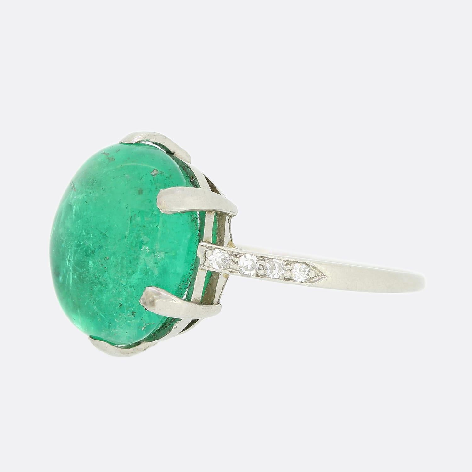 This is a vintage platinum emerald and diamond ring. The rare Columbian emerald is natural with moderate oil enhancement and is a cabochon cut with a highly desirable rich green tone. The emerald is claw set, has four single cut diamonds on each