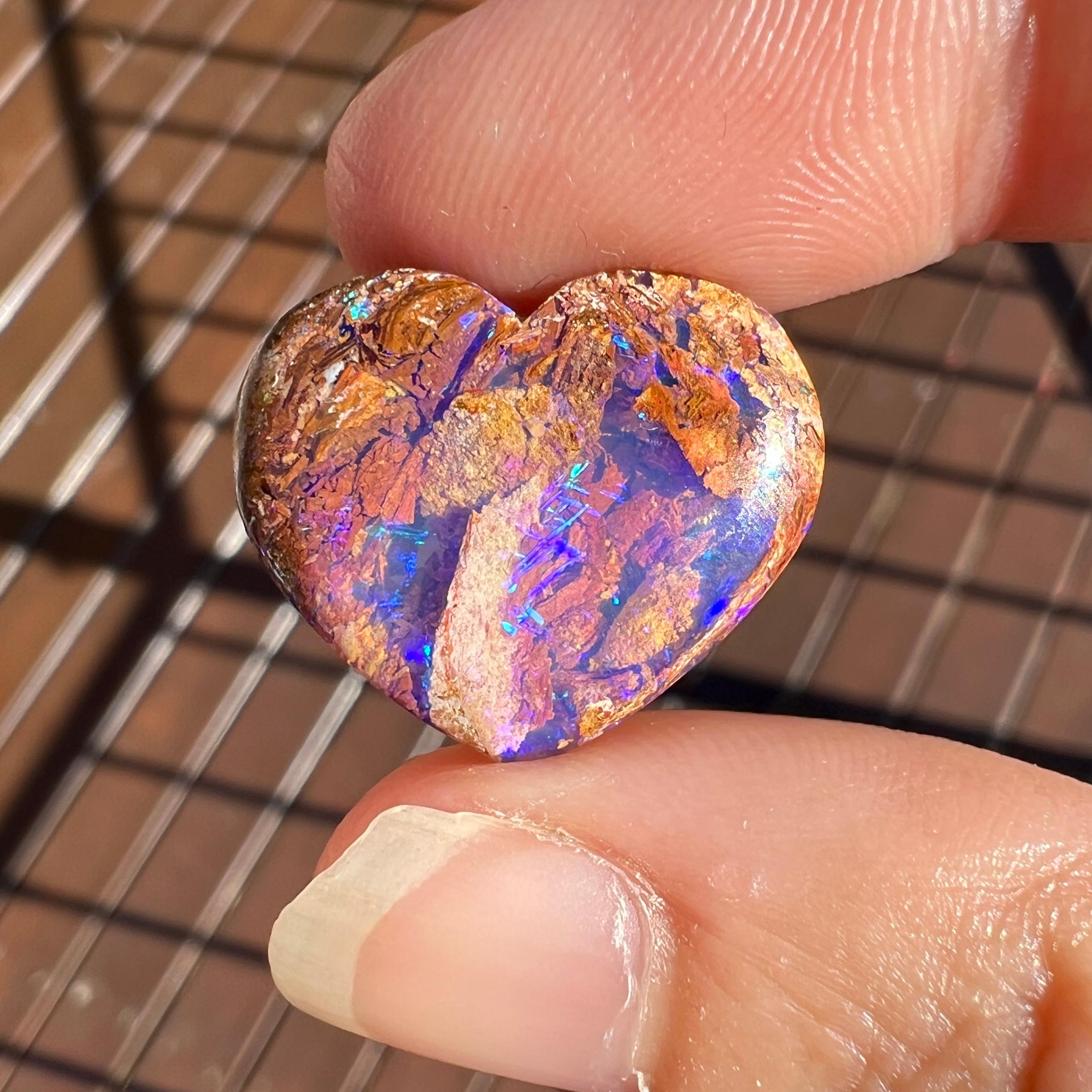 This brilliant 9.36 Ct wood replacement opal, carved into a heart, is a truly exceptional addition to any collection, mined by Sue Cooper herself. Its rarity, coupled with its modern form, captivates connoisseurs with its vibrant play of purples,