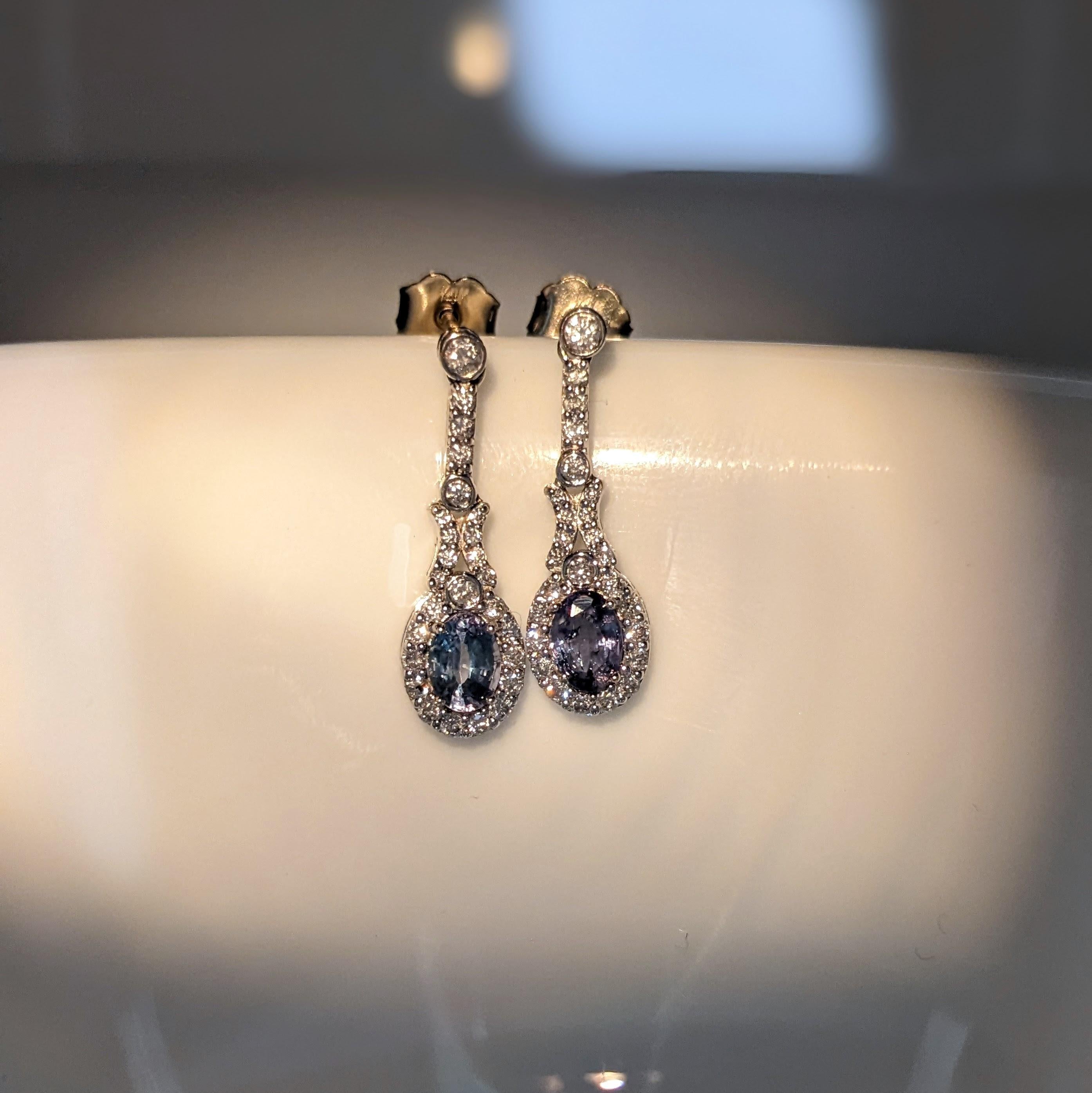 These beautiful dangle earrings feature a pair of 0.77 carat weight natural Alexandrite gemstones with natural earth mined diamonds set in solid 14K gold. The color changing natural alexandrite appears blue green in daylight and shifts to a deep