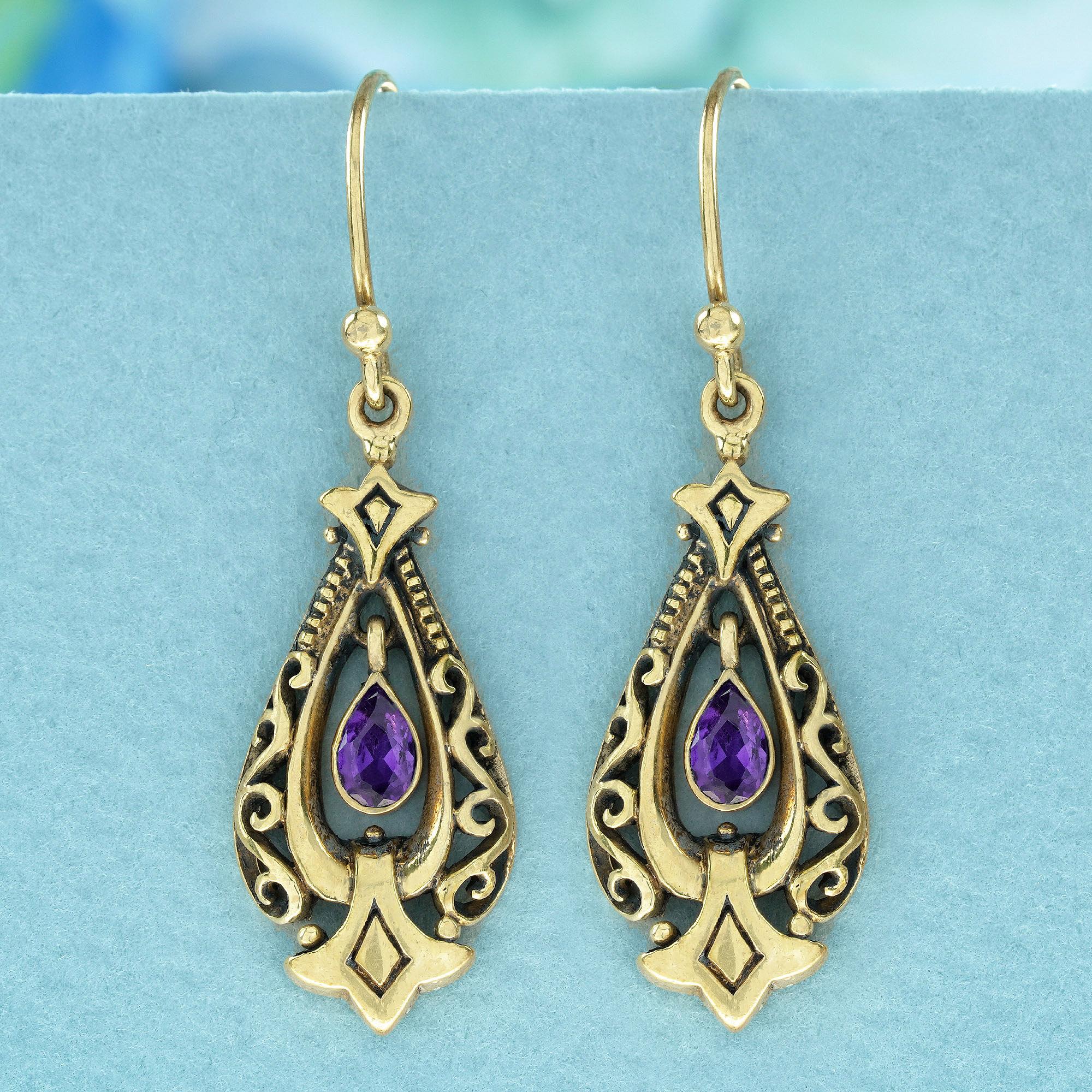 Crafted in vintage-style drop design, these yellow gold earrings feature a purple drop shaped amethyst at the center surrounded by delicate yellow gold scrollwork. The dangle design is completed with a hook closure at the top, adding a touch of