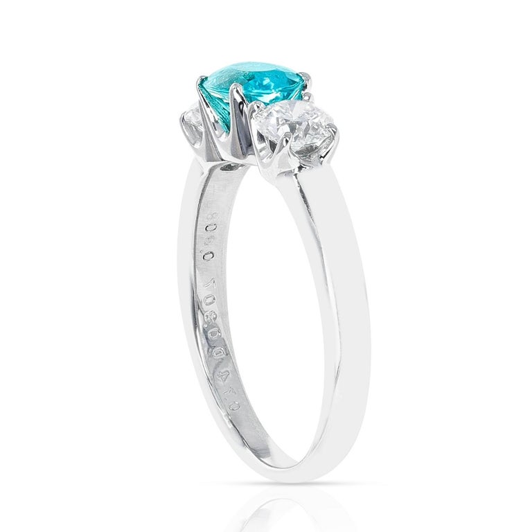 An elegant and chic three-stone platinum ring, set with a natural, certified, and beautiful oval-shaped mixed-cut electric-blue Paraiba tourmaline weighing 0.74 carats, accented with two round brilliant-cut diamonds weighing a total of approximately