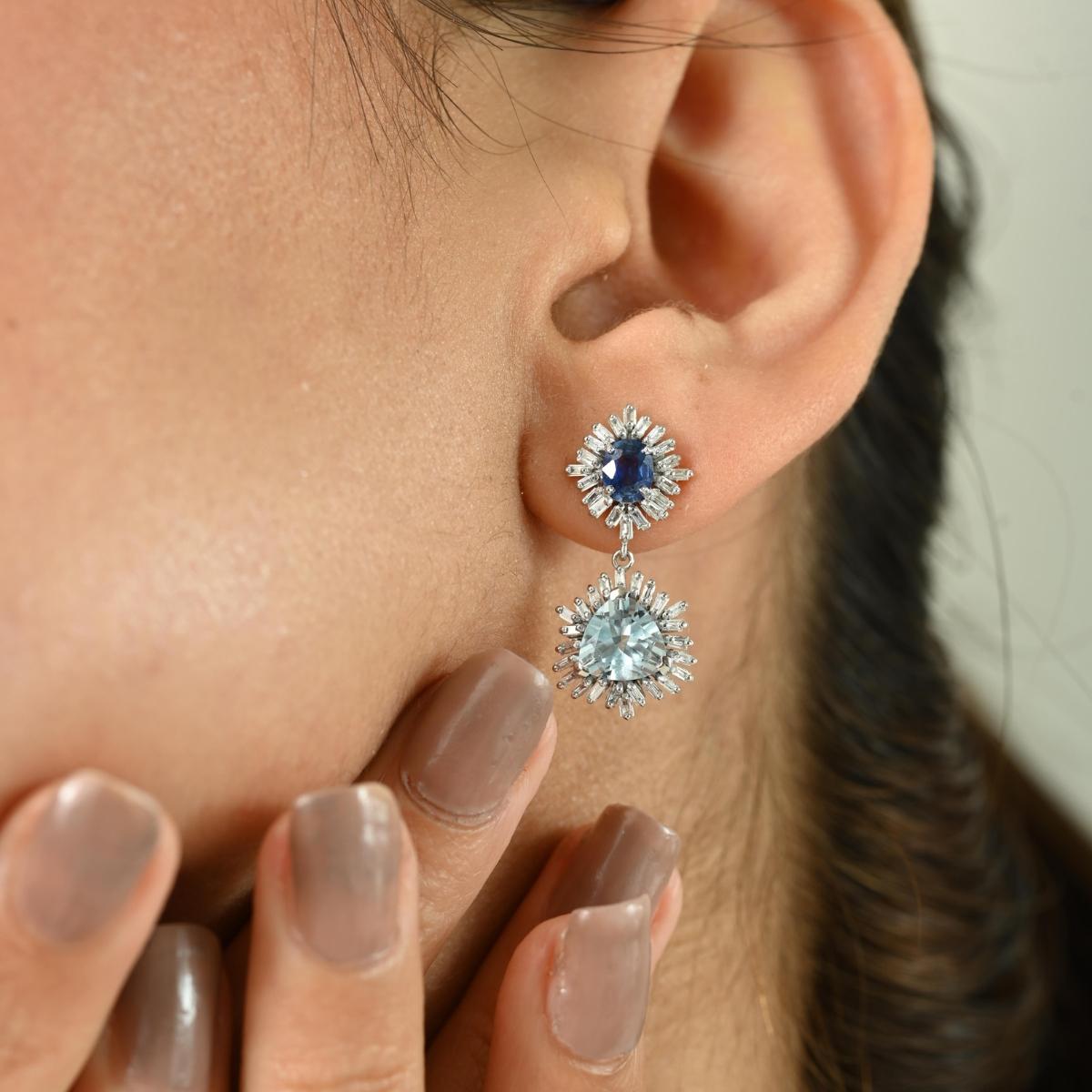 Radiating a celestial charm, these exquisite drop earrings are crafted in luminous 14k white gold and adorned with a striking combination of gemstones. At the top, a vivid round-cut blue sapphire takes center stage, encircled by a dazzling starburst