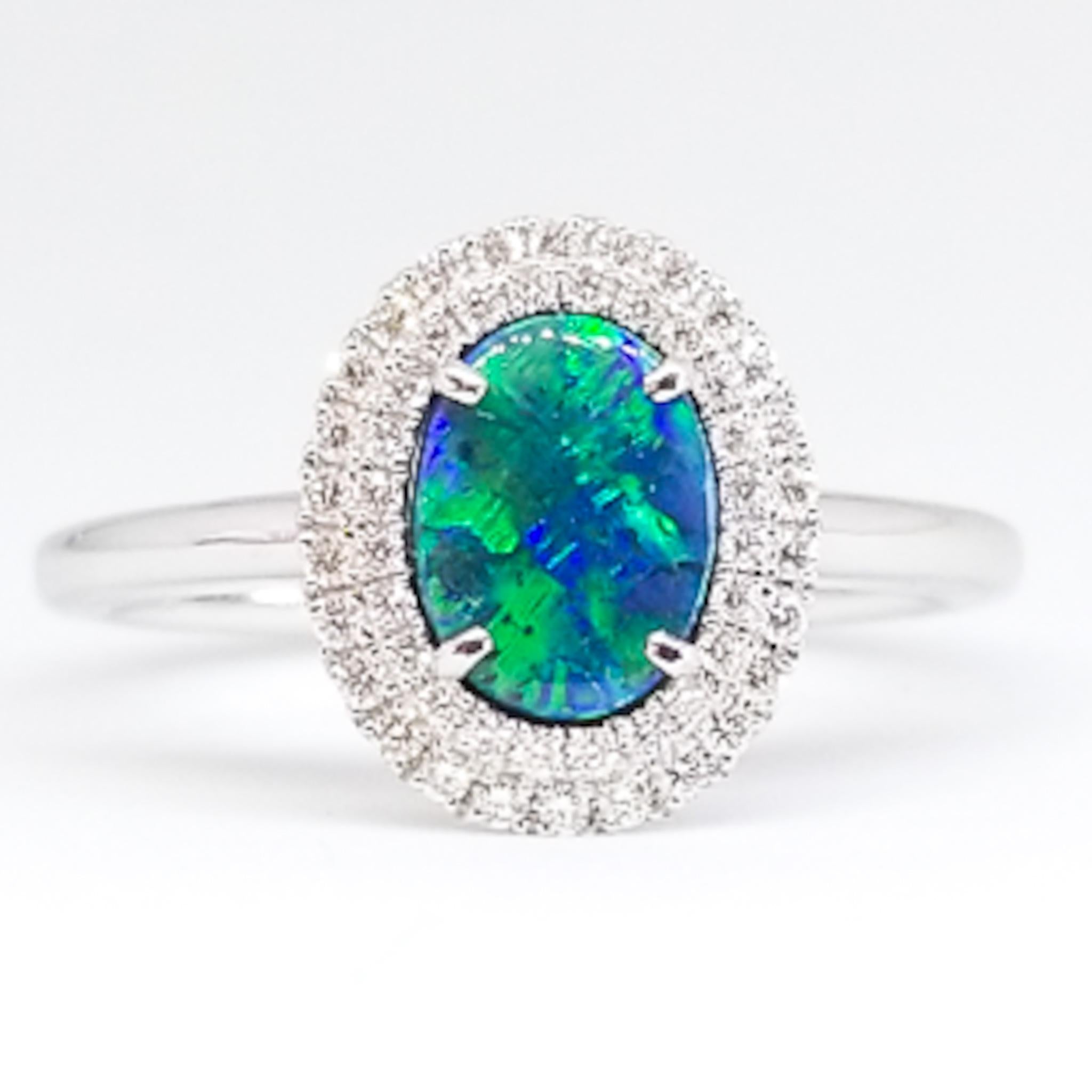A Contemporary Engagement, Promise or Birthstone Ring is set with a 0.51 Carat Oval, Natural Australian Black Opal with Deep Color Saturation and Light Play. The Gem Quality stone shows fire of Blues and Greens and is set in prongs, surrounded by a