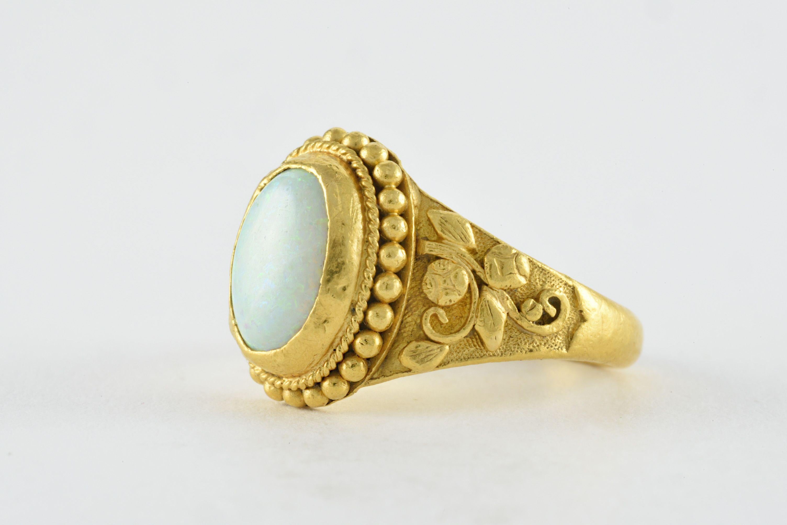 An oval-shaped natural Australian opal measuring 9mm x 7mm is the centerpiece of this beautiful band crafted from 22kt yellow gold and embellished with elaborate hand engraving. 