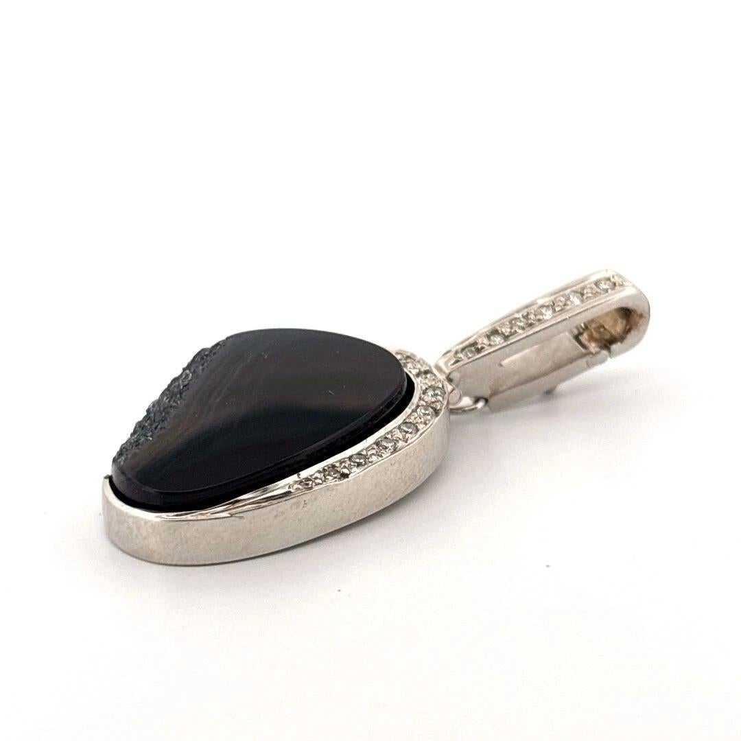 This unique and bold black agate druzy pendant is crafted in solid 14K white gold, featuring an oval freeform druzy stone accented by a curved row of natural round brilliant-cut diamonds along the edge and up the bail. The druzy surface sparkles