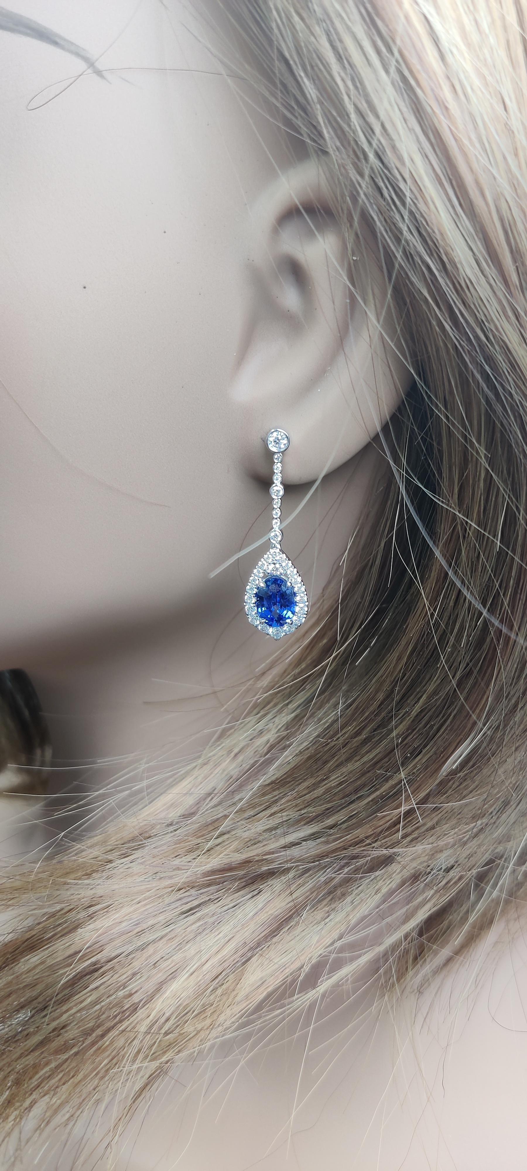 RareGemWorld's classic sapphire earrings. Mounted in a beautiful 18K White Gold setting with natural oval cut blue sapphires. The sapphires are surrounded by natural round white diamond melee. These earrings are guaranteed to impress and enhance