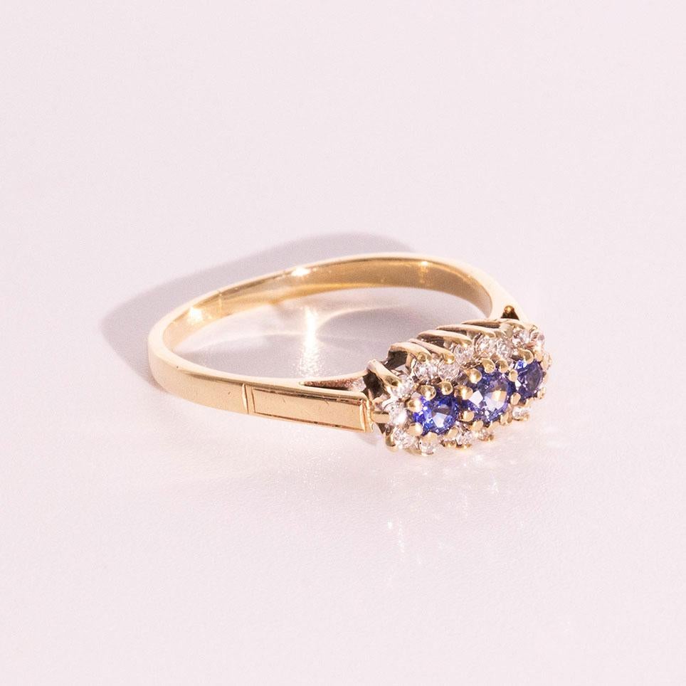 Lovingly crafted in 9 carat gold is this enchanting vintage ring featuring a cluster of three bright natural blue round sapphires encompassed by a total of 0.13 carats of sparkling round diamonds. We have named this piece of vintage splendour The