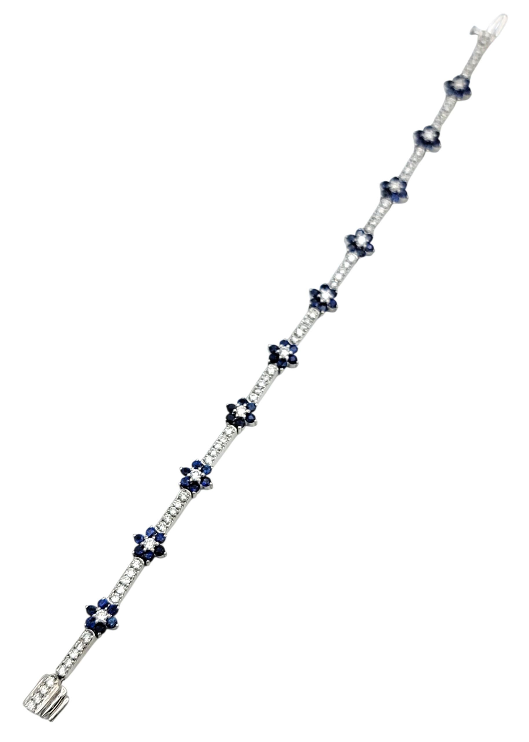This exquisite white gold bracelet features an alternating pattern of sparkling flower clusters and curved diamond links, forming a continuous floral motif across the wrist. The elegant design pairs natural diamonds with vivid blue sapphires, each